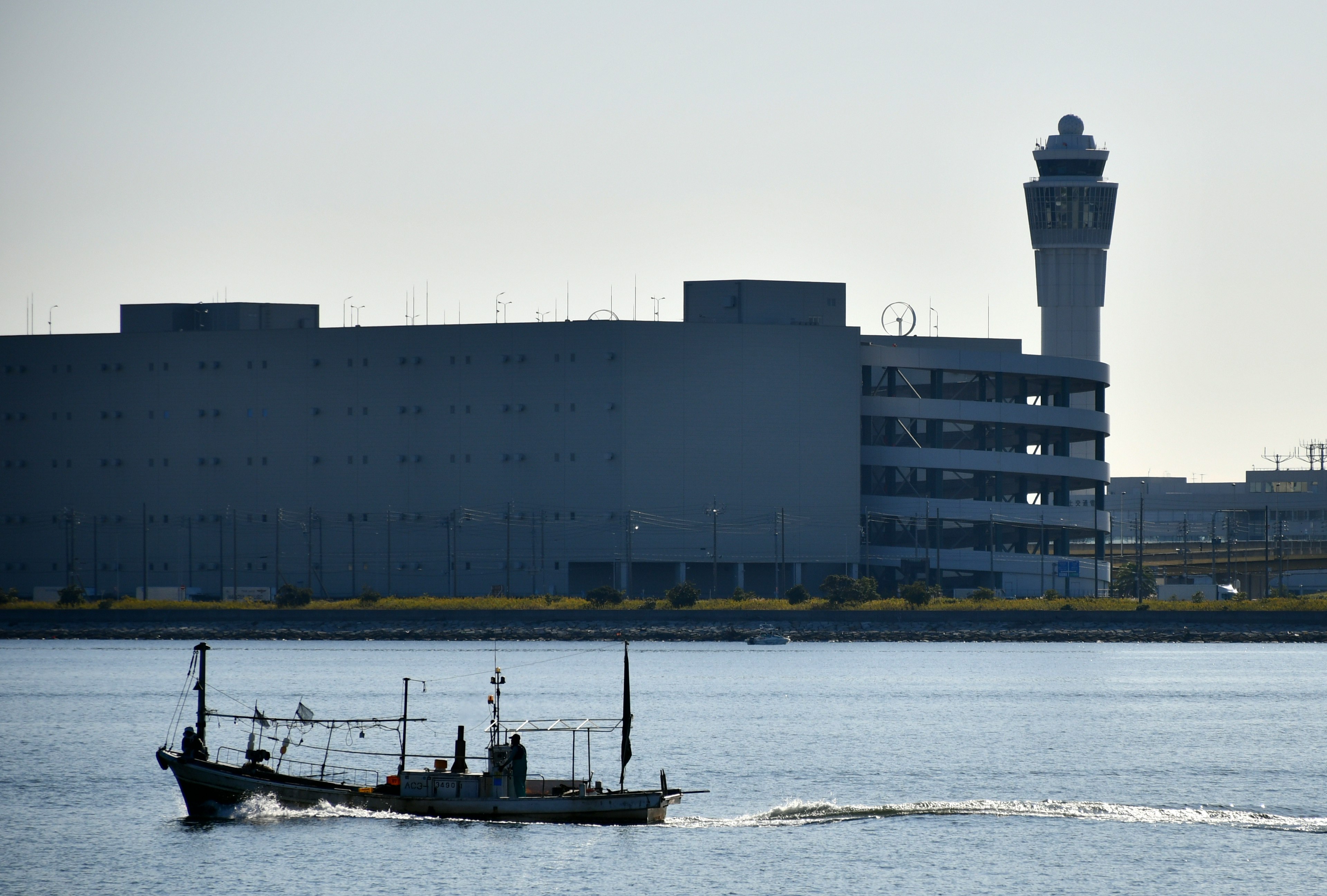 Barco pesquero navegando en el agua con una torre de aeropuerto al fondo