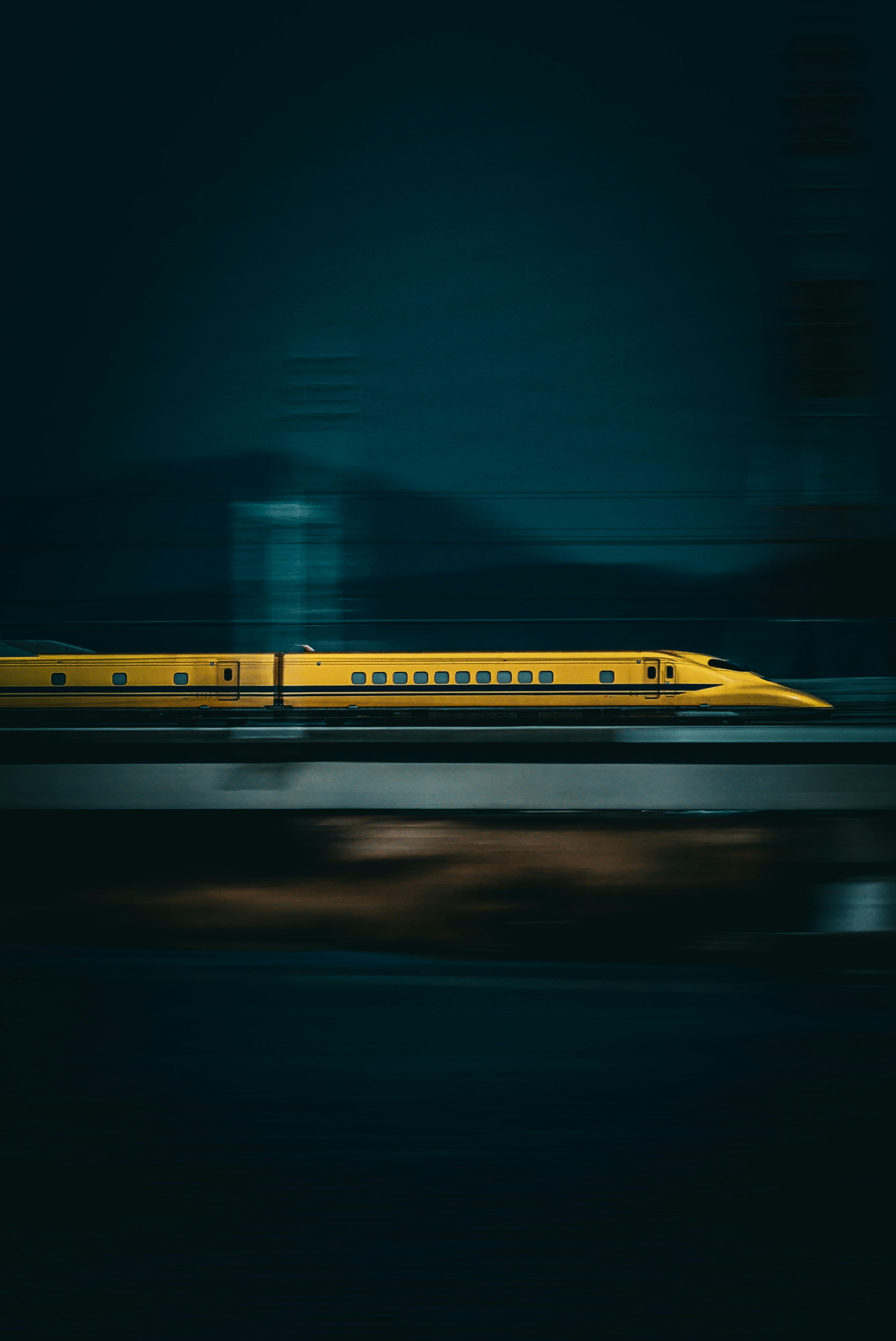 Yellow Shinkansen train speeding past in a dark setting