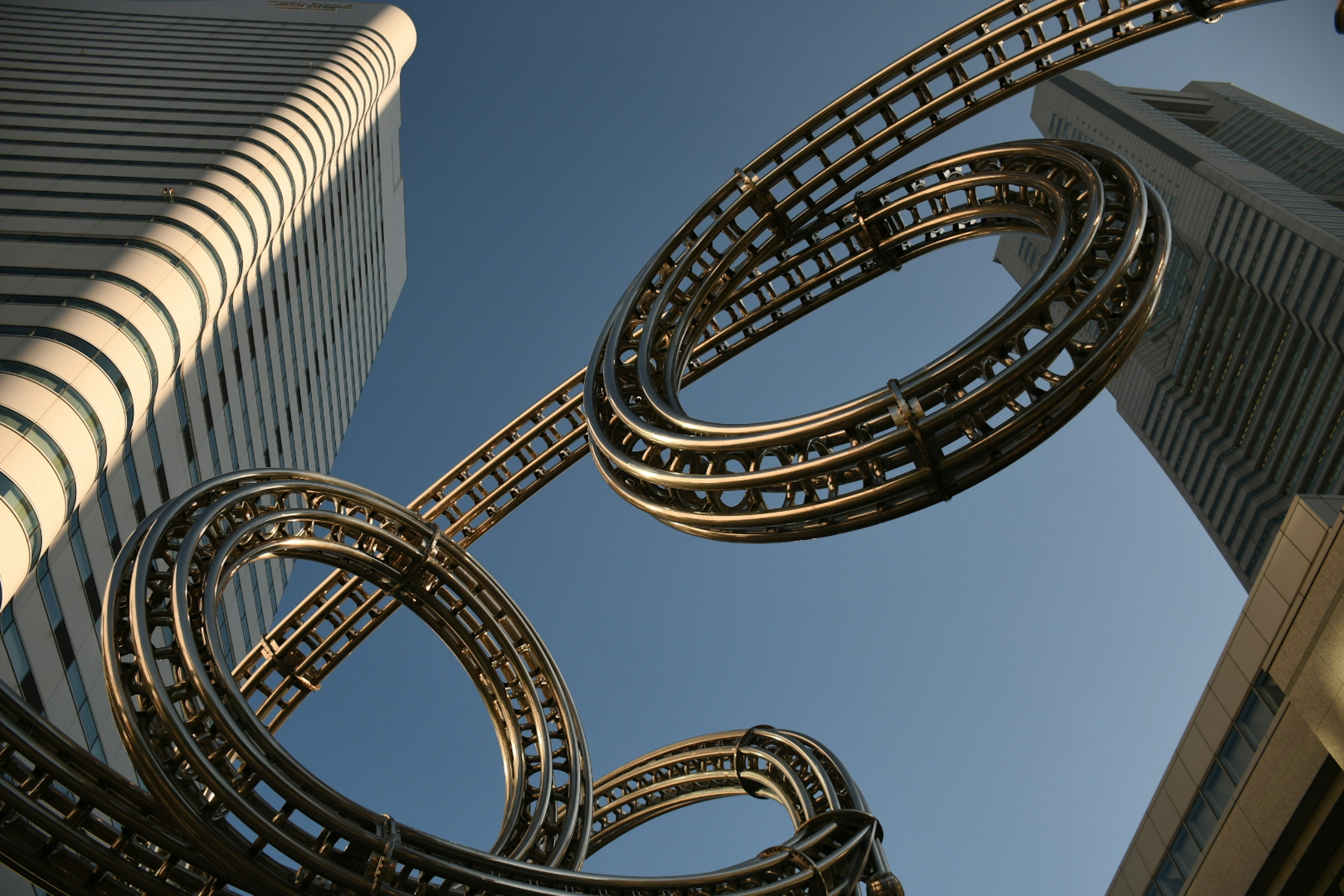 Sculpture métallique unique se tordant entre des gratte-ciels sous un ciel bleu clair