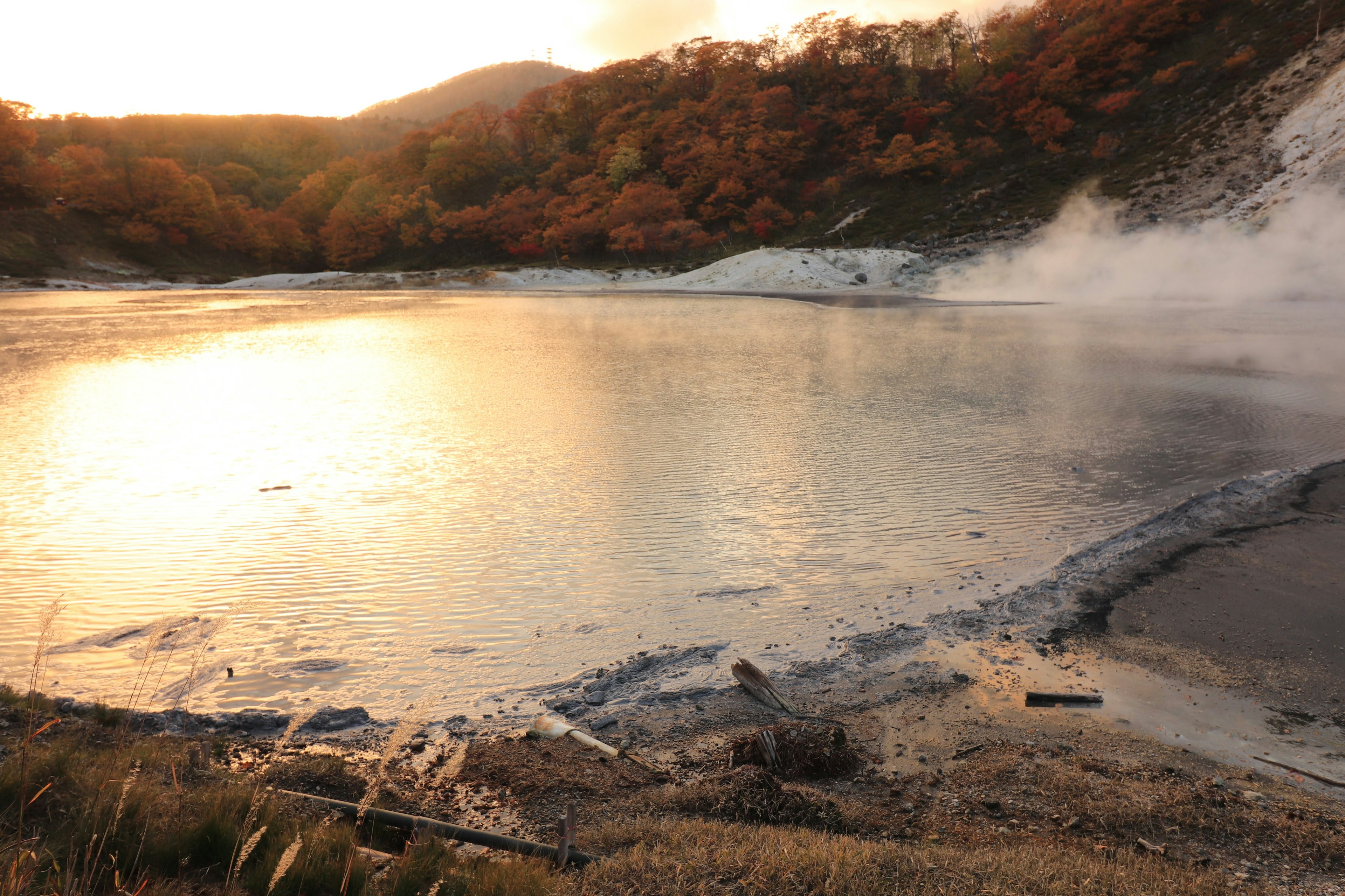 Vista escénica de una fuente termal con una superficie de agua tranquila y follaje otoñal al atardecer