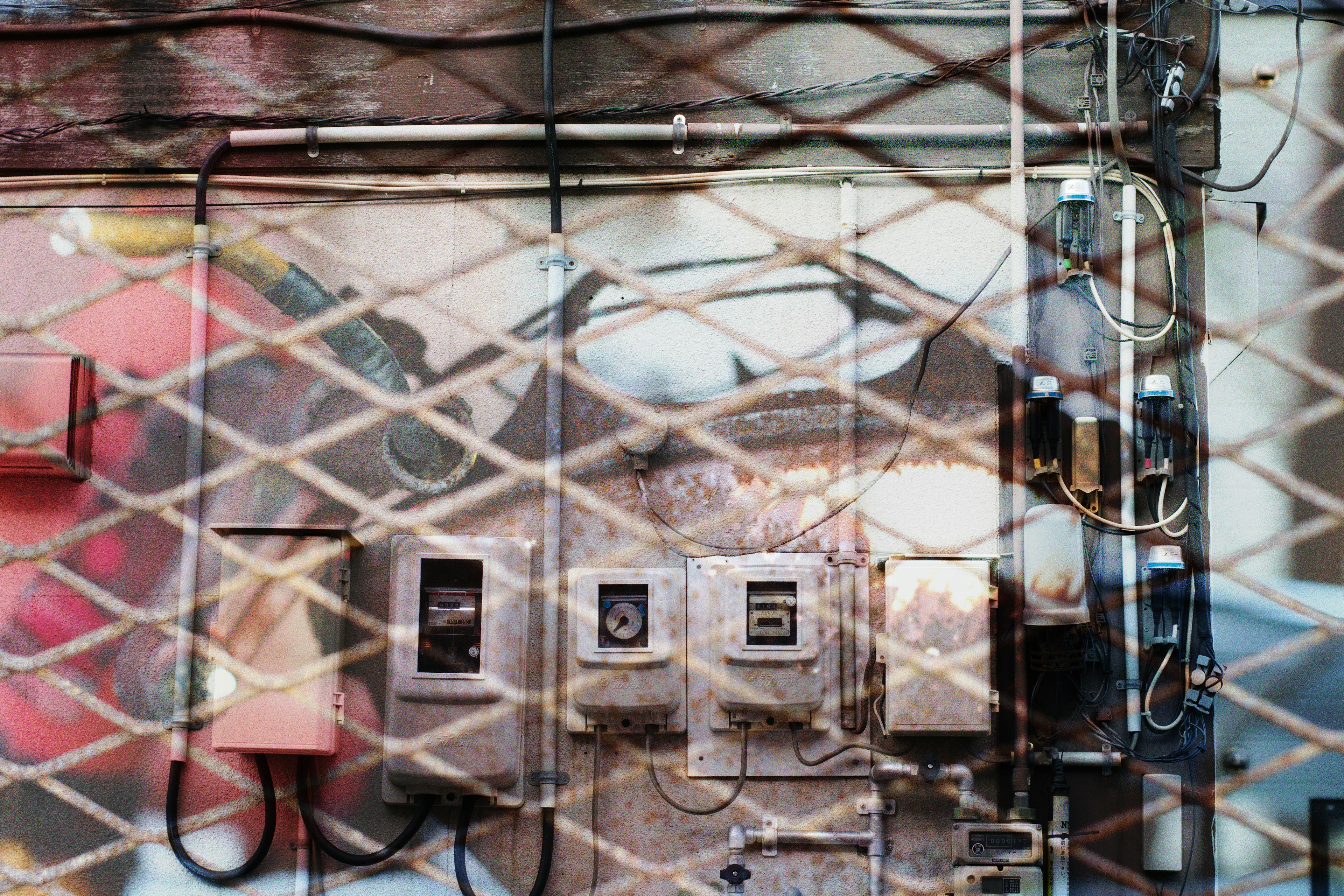 Wall with old electrical boxes and wiring seen through a mesh fence