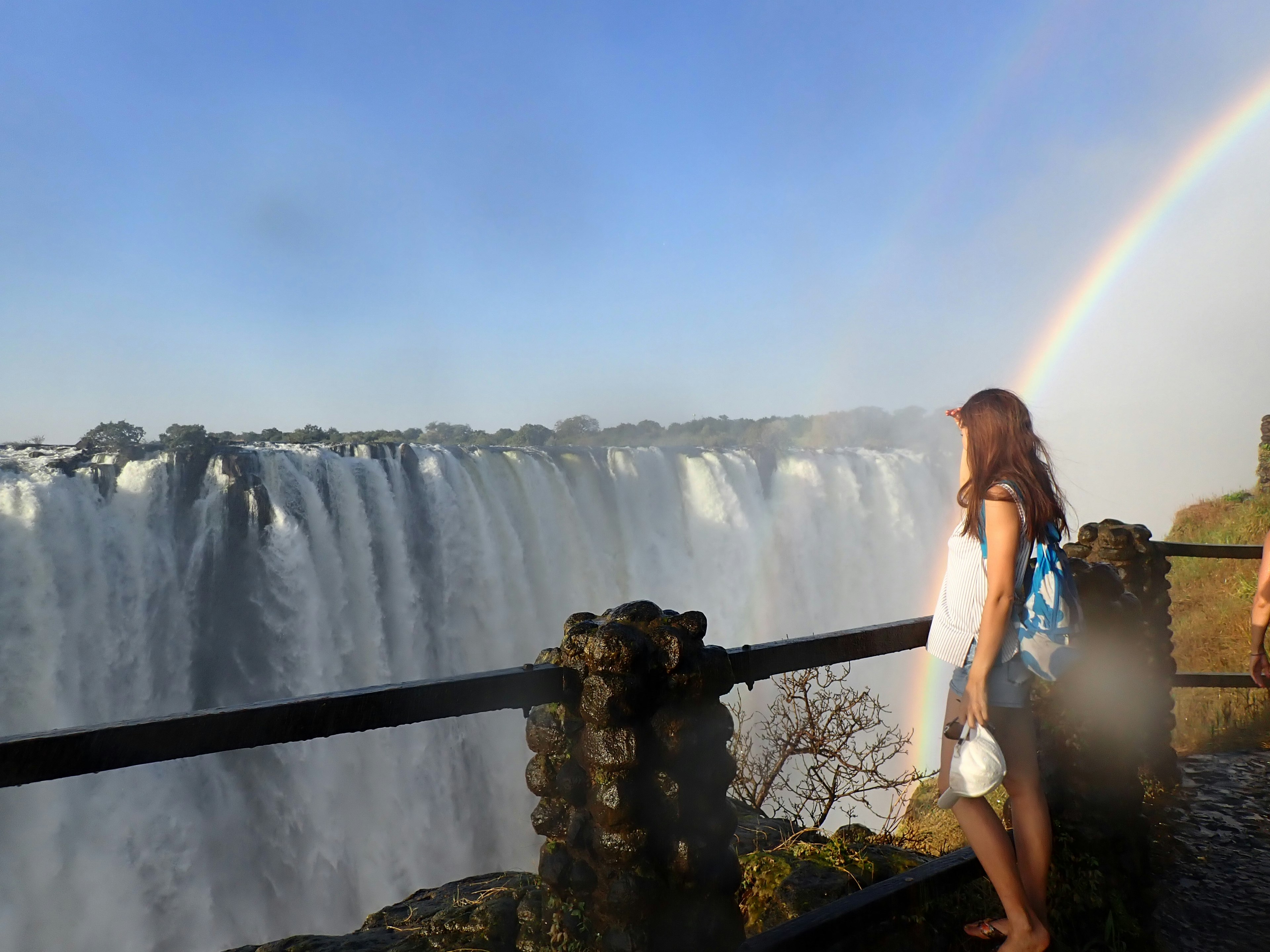 Silhouette einer Frau, die einen Wasserfall mit einem Regenbogen betrachtet