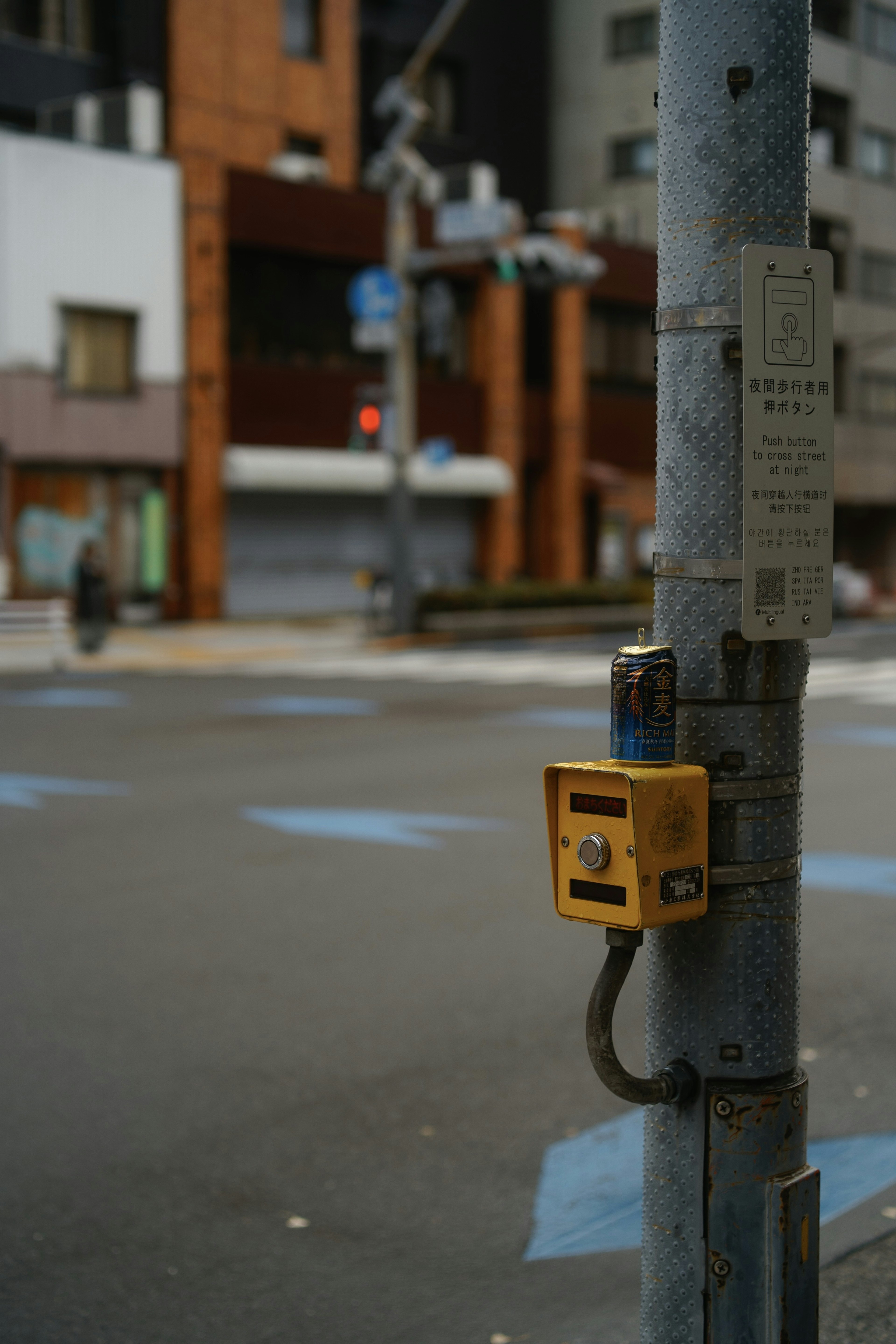 交差点の信号機の近くにある黄色い押しボタンと街の建物