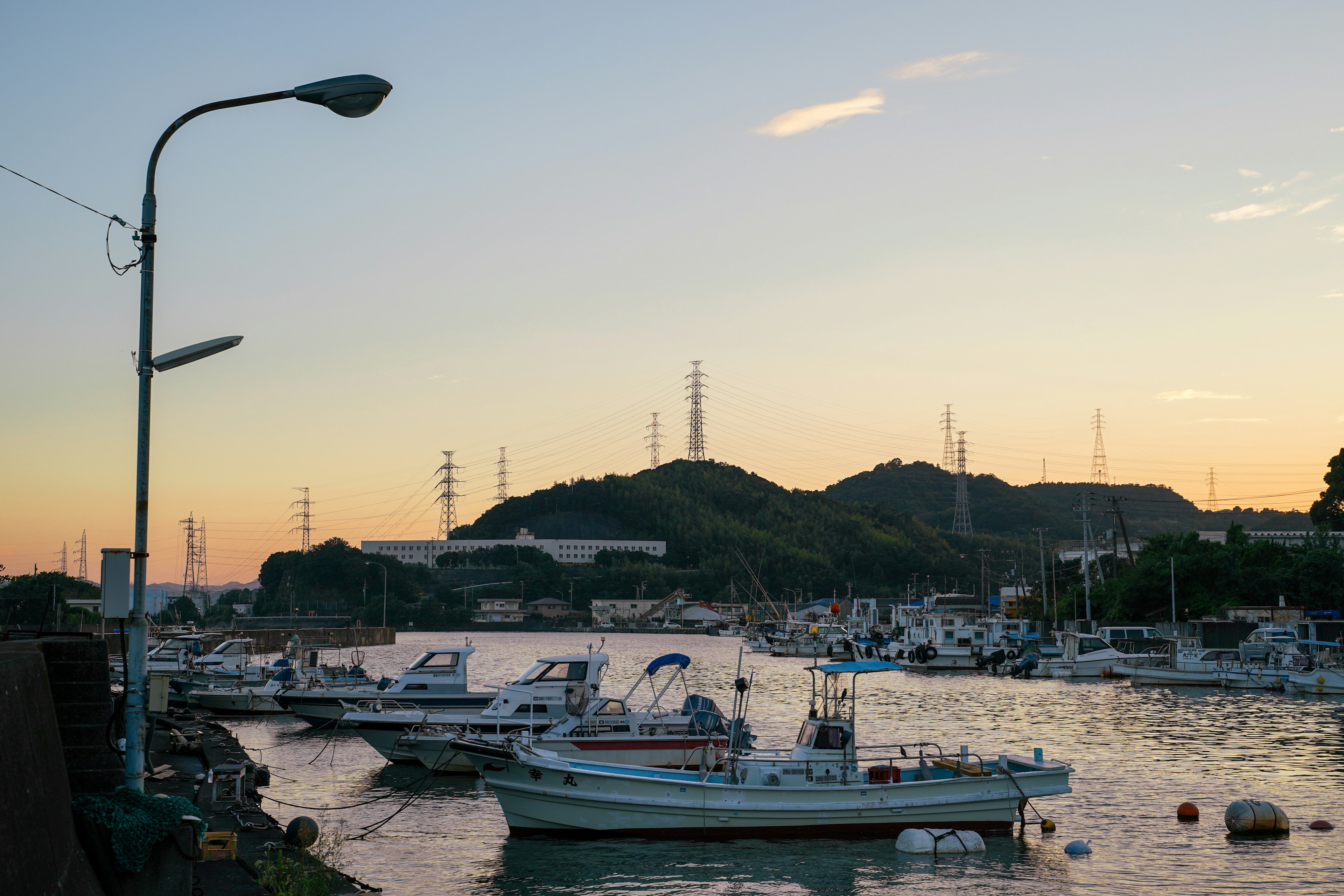 Barche ormeggiate nel porto al tramonto con silhouette di montagna