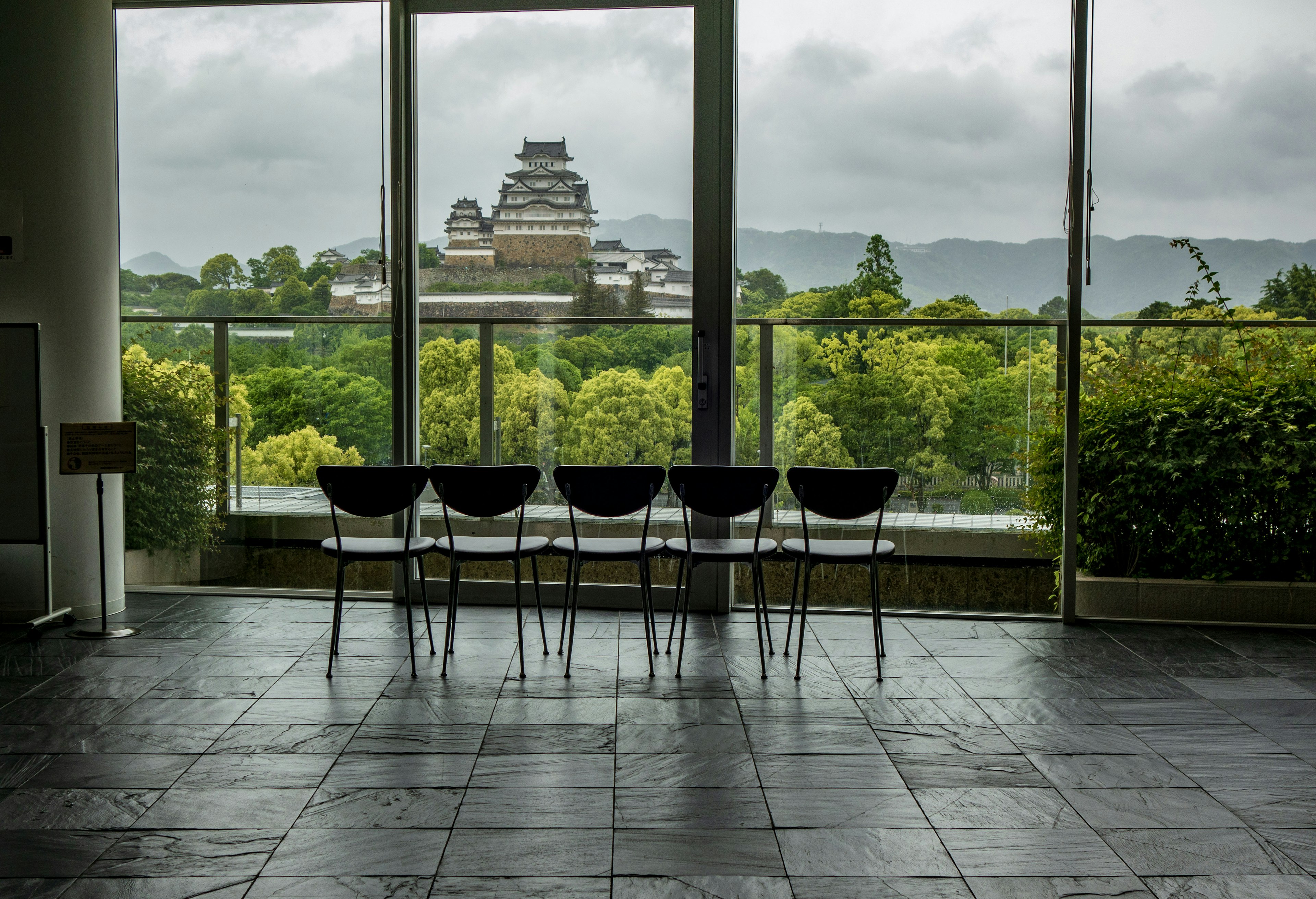 Modernes Interieur mit schwarzen Stühlen in Reihe und Blick auf üppiges Grün und eine schlossartige Struktur im Hintergrund