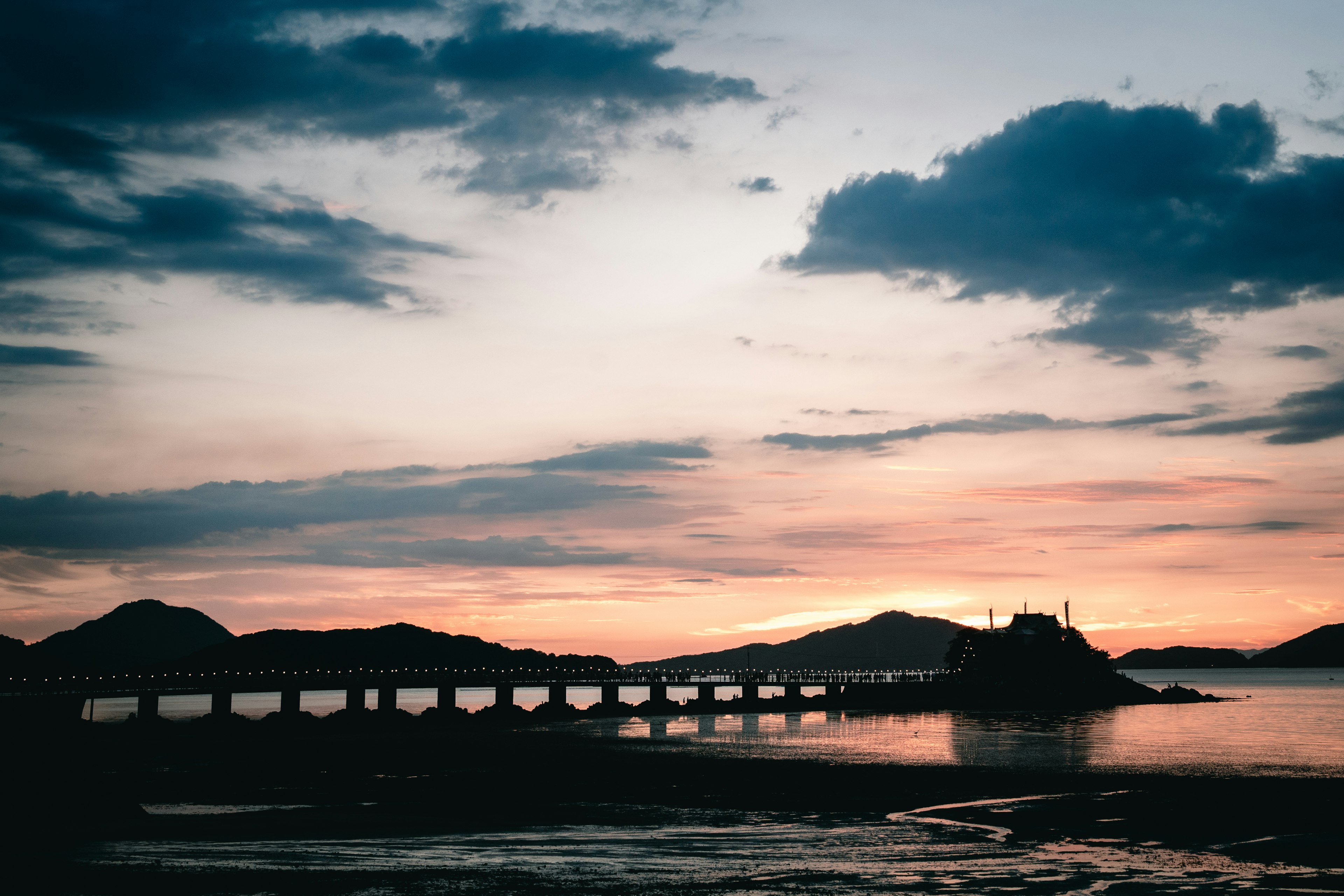 Silhouette di un ponte sul mare al tramonto con montagne sullo sfondo