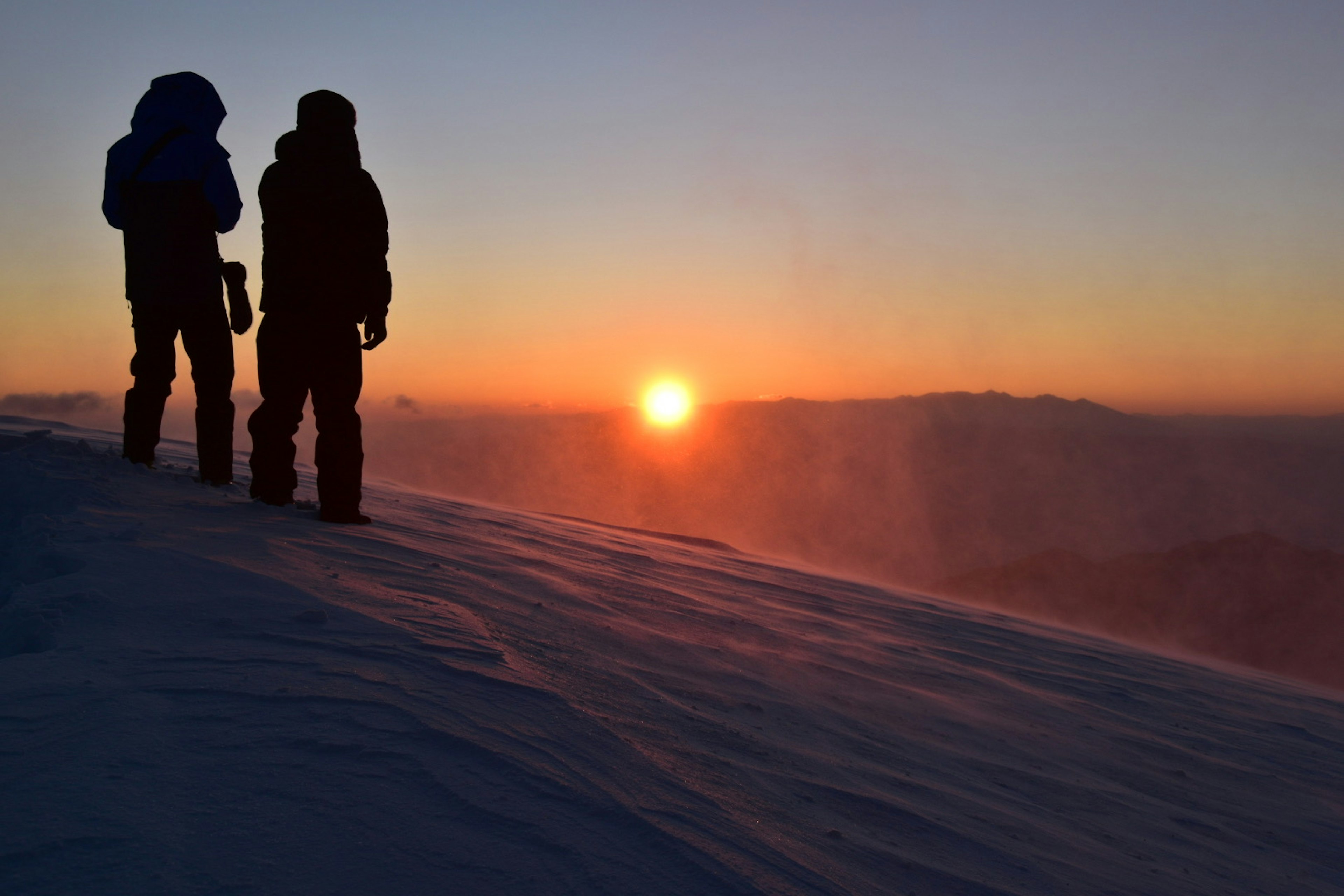 Silhouette di scalatori sulla cima innevata che osservano il tramonto