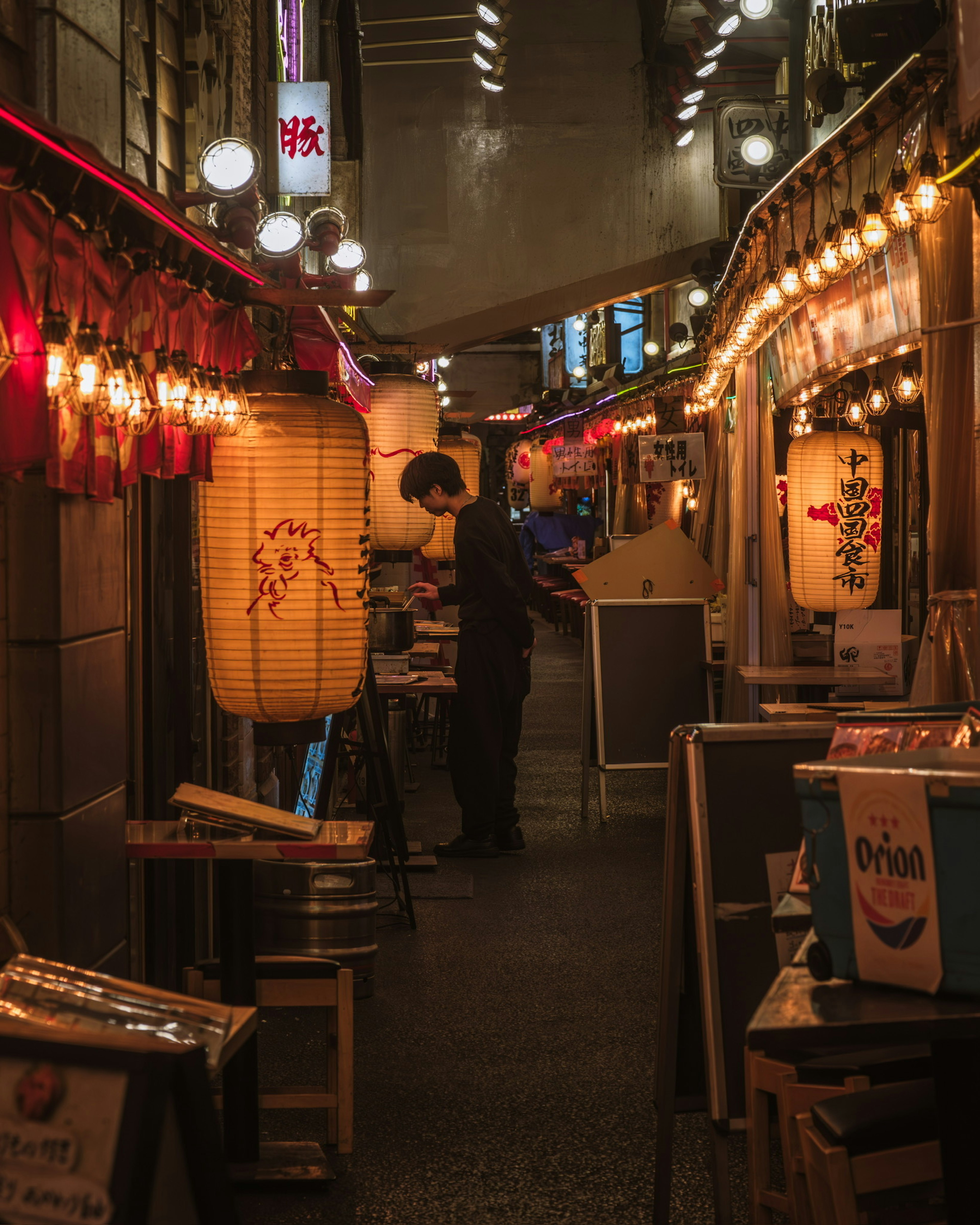 A person in a narrow alley lined with lanterns and warm lights of restaurants