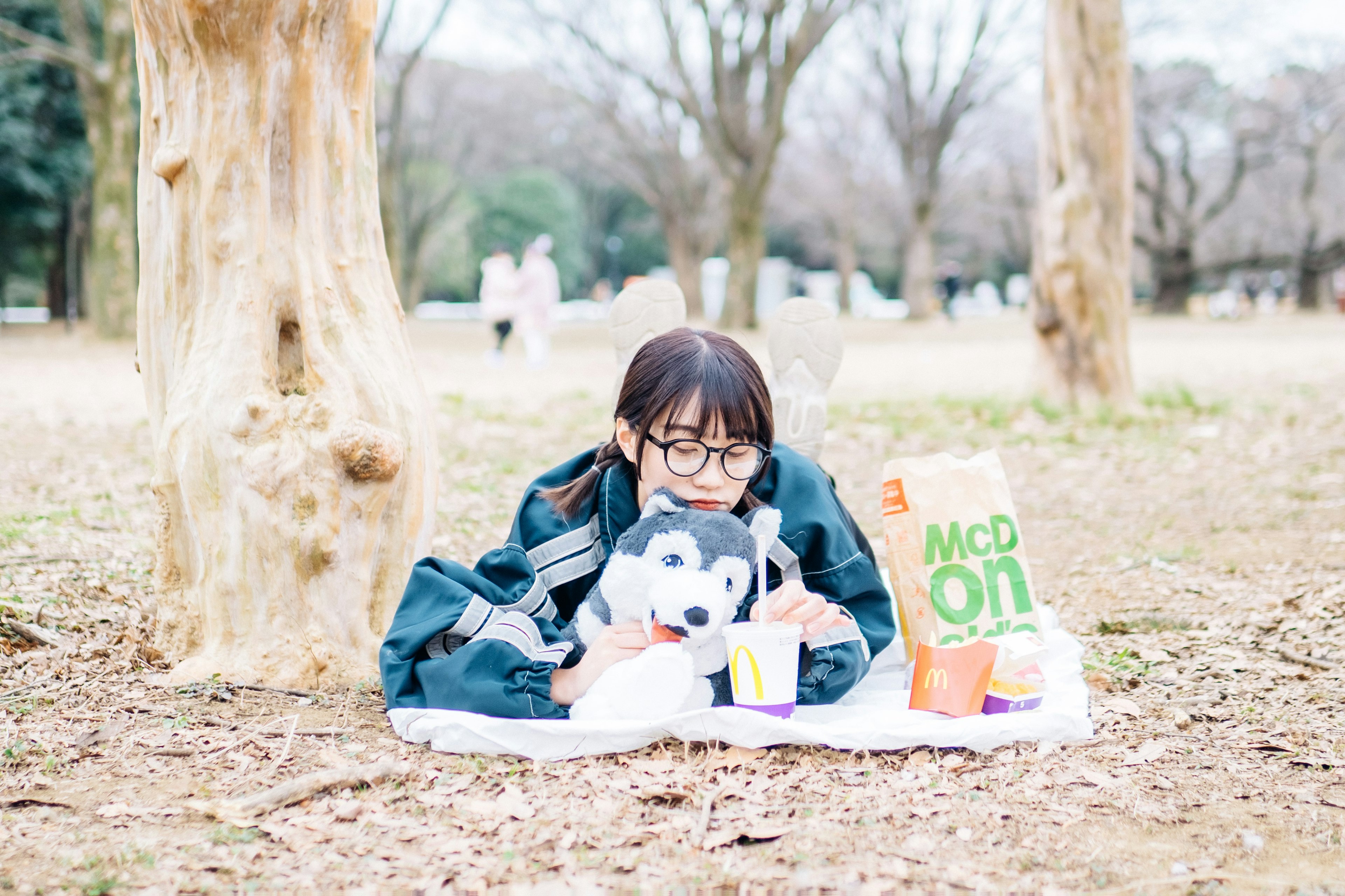 Chica relajándose en el parque con un husky de peluche y una bolsa de McDonald's