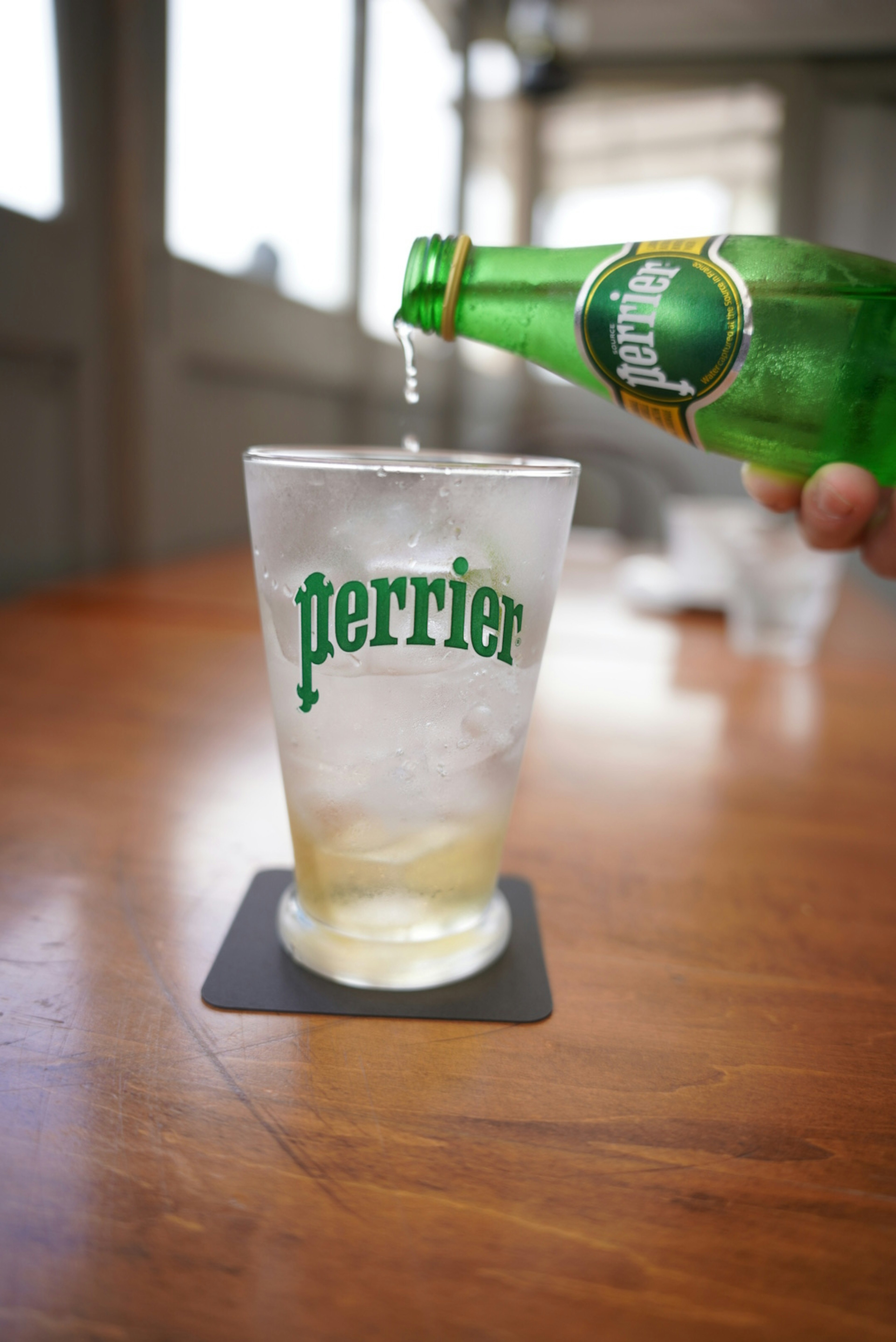 Main versant de l'eau Perrier dans un verre sur une table en bois