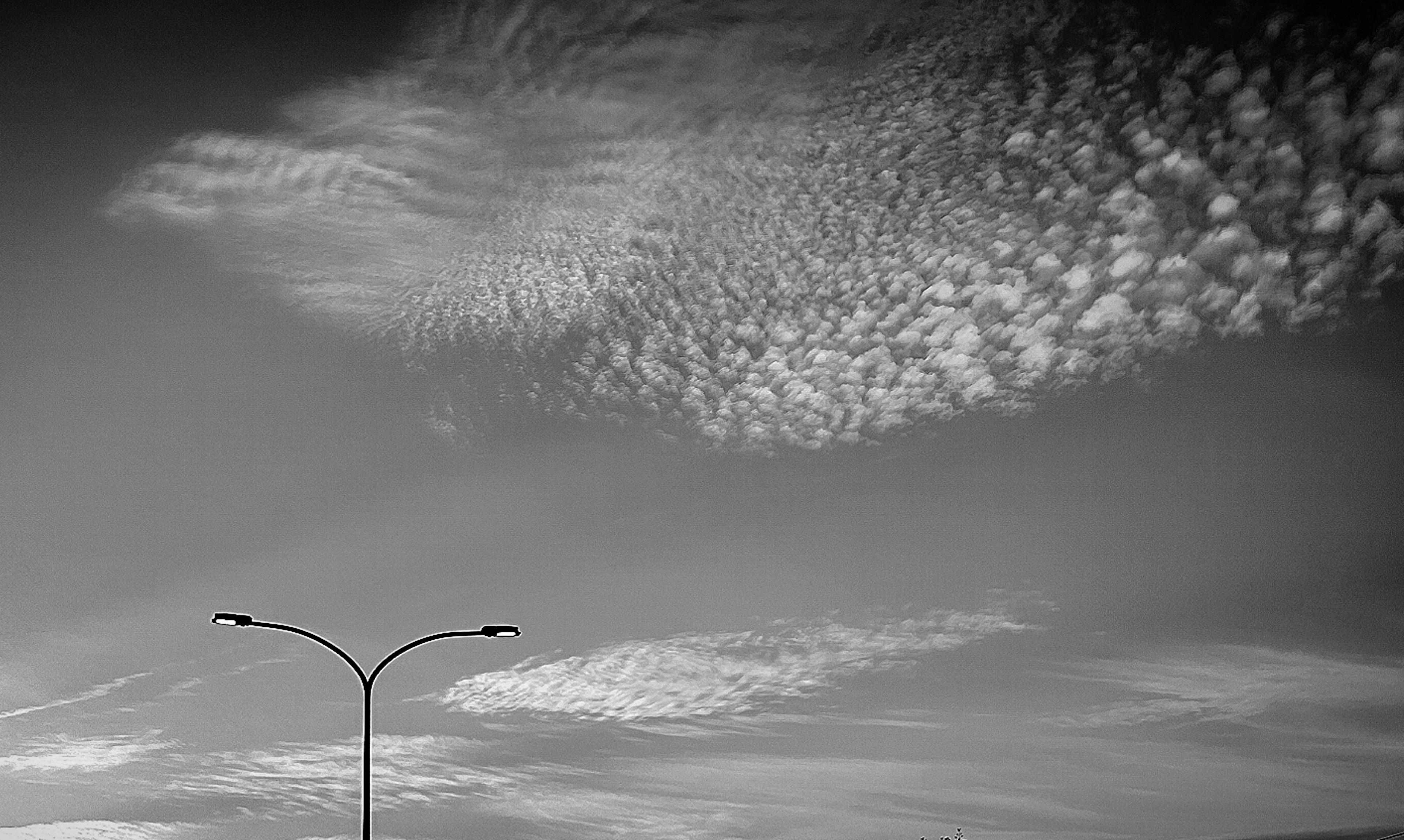 Gambar hitam putih dengan awan tidak teratur di langit dan lampu jalan