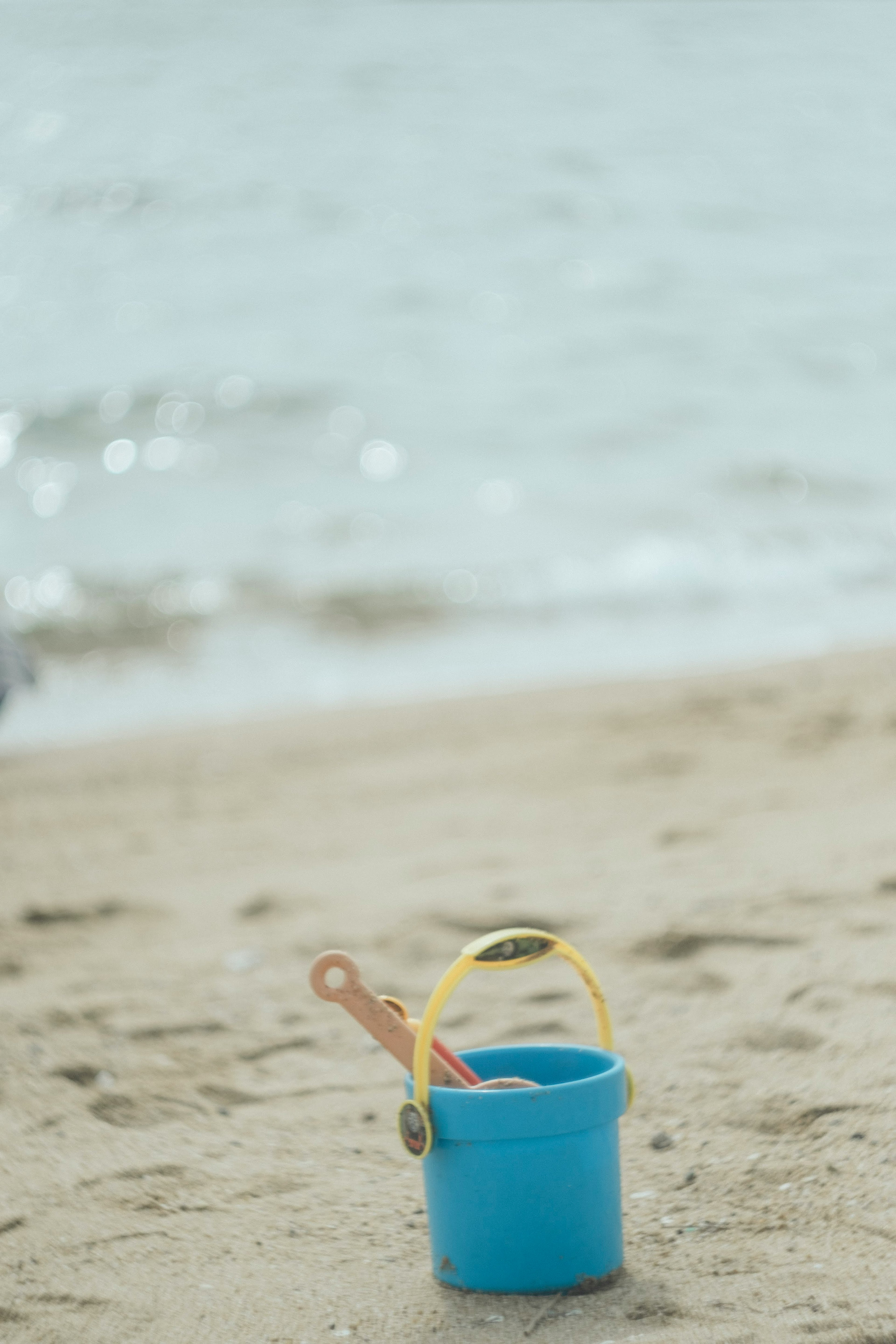 ถังน้ำสีฟ้ากับพลั่วบนชายหาดทรายมีมหาสมุทรอยู่เบื้องหลัง