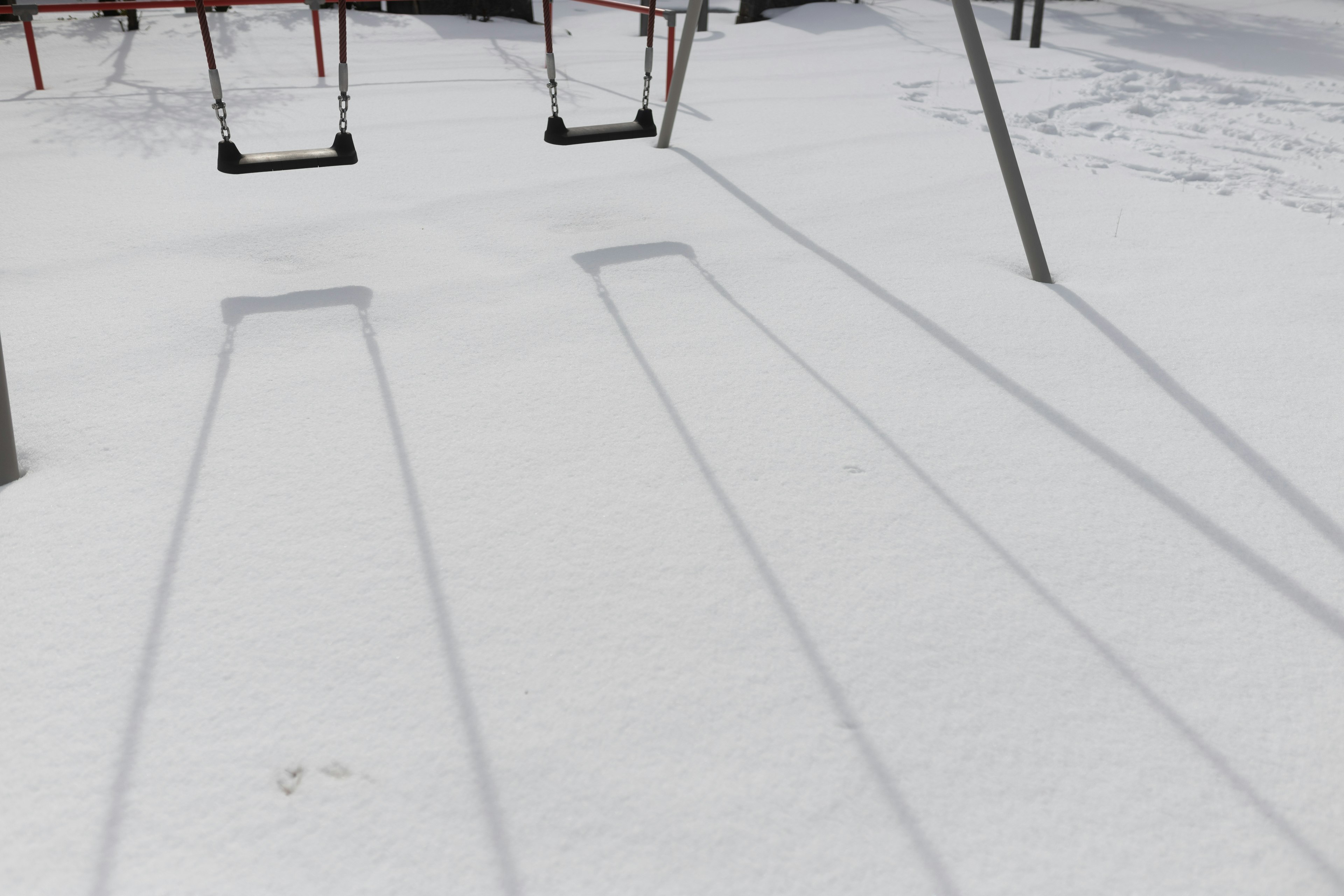 Swings in a snowy playground with long shadows