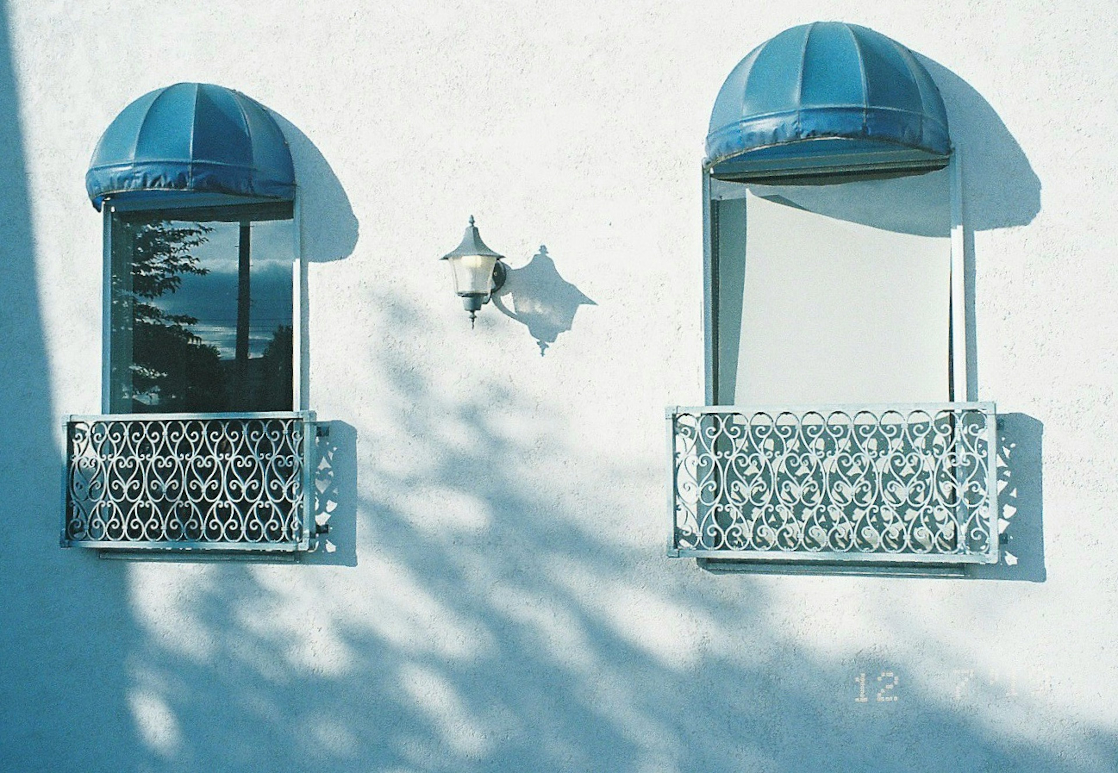 Due finestre con awning blu su una parete bianca con ringhiere decorative in metallo