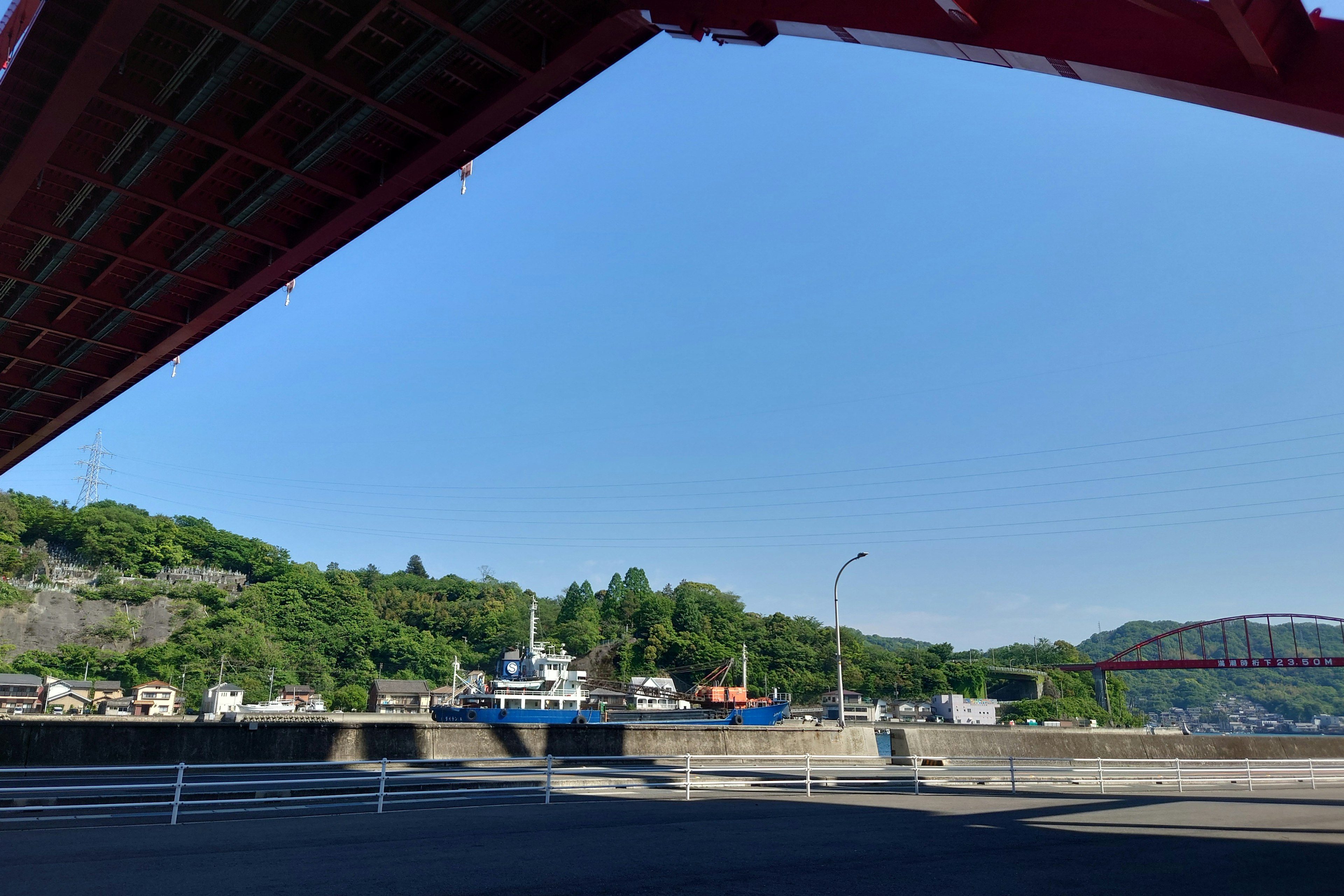 Vista de un puerto bajo un puente rojo con barcos y colinas verdes