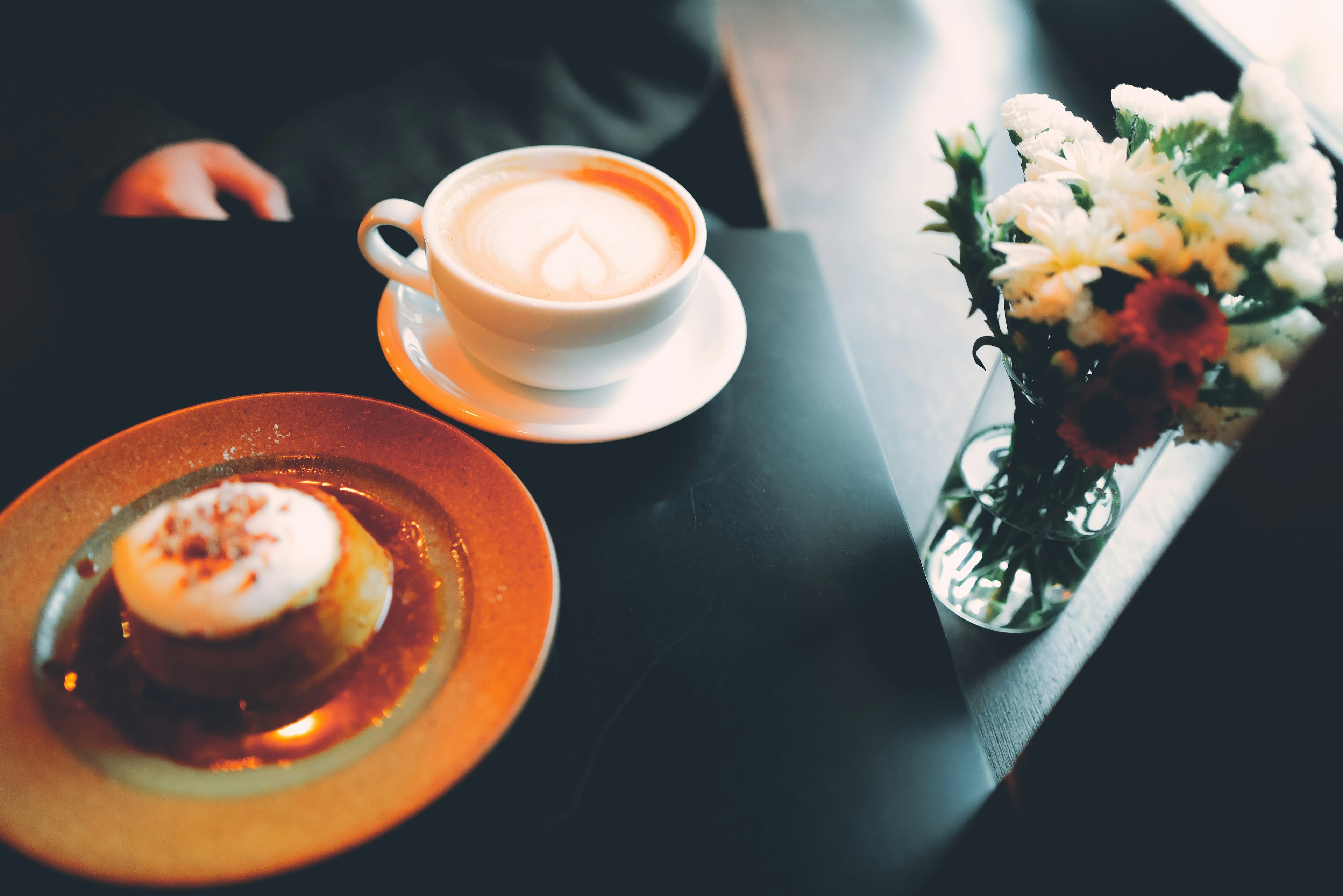 Ein Cafétisch mit einer Tasse Kaffee und einem Dessertteller sowie Blumen in einer Vase