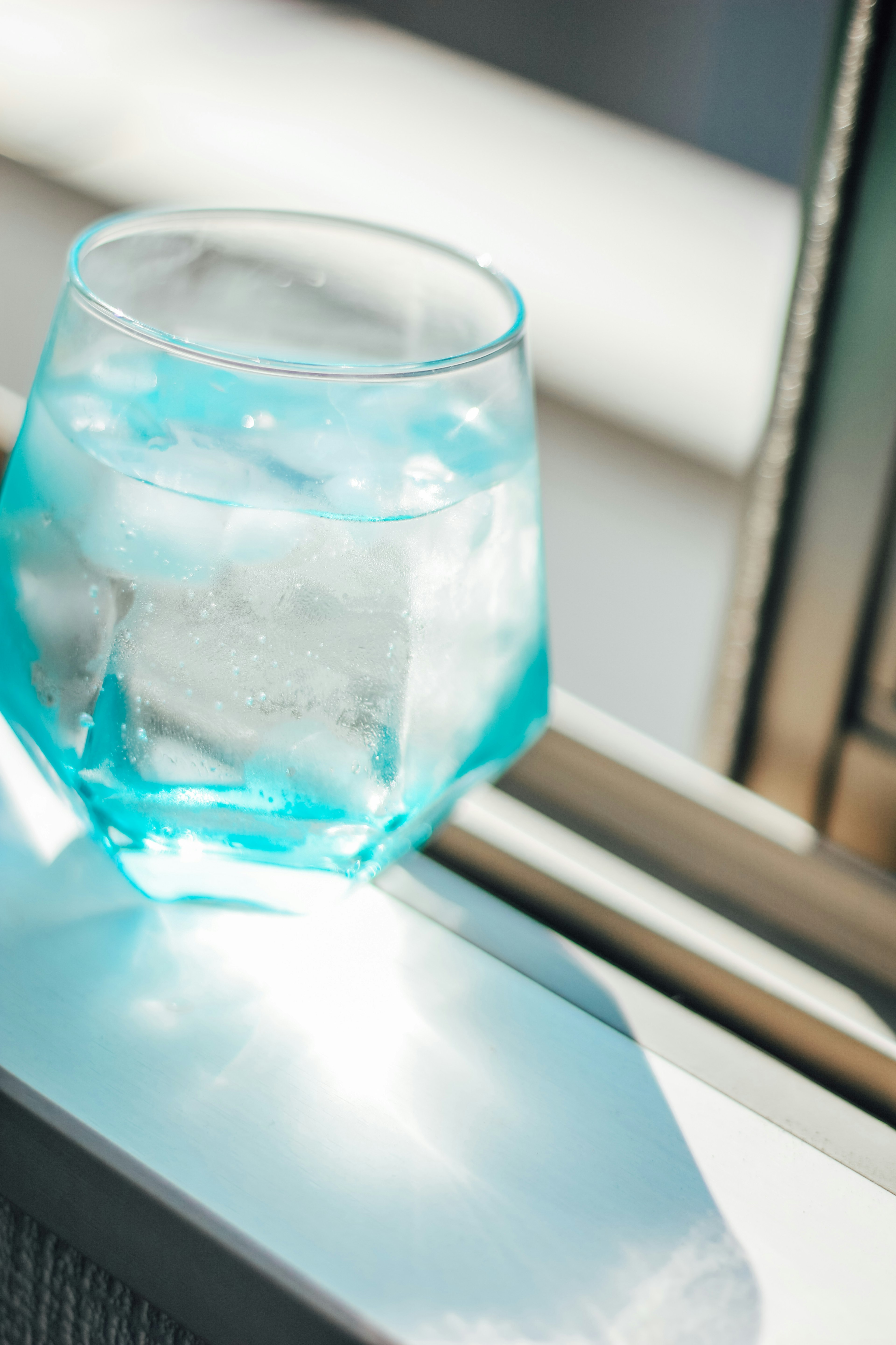 Un vaso azul con agua con hielo colocado en un alféizar de ventana