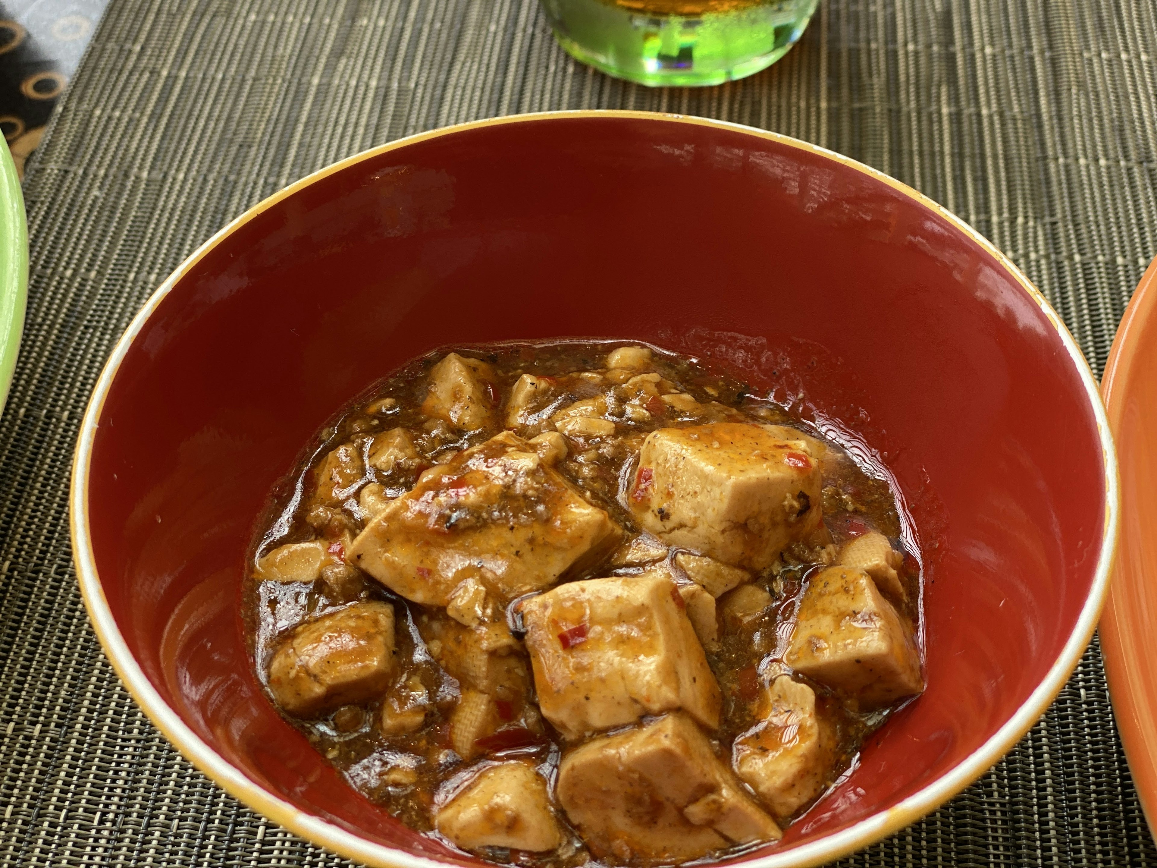 Plat de tofu dans un bol rouge avec une sauce foncée et de gros cubes de tofu