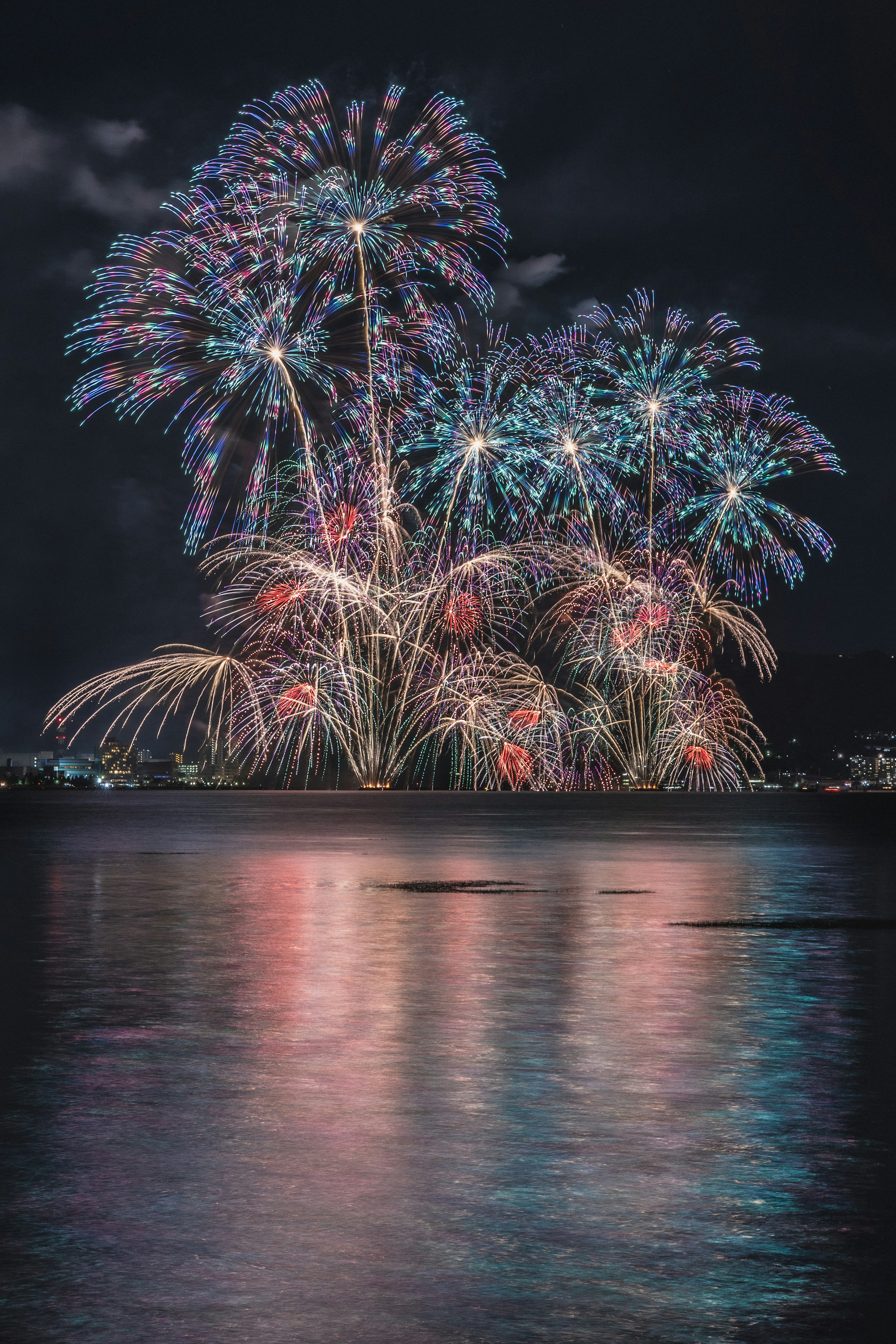 Fuochi d'artificio colorati che esplodono nel cielo notturno con riflessi sull'acqua