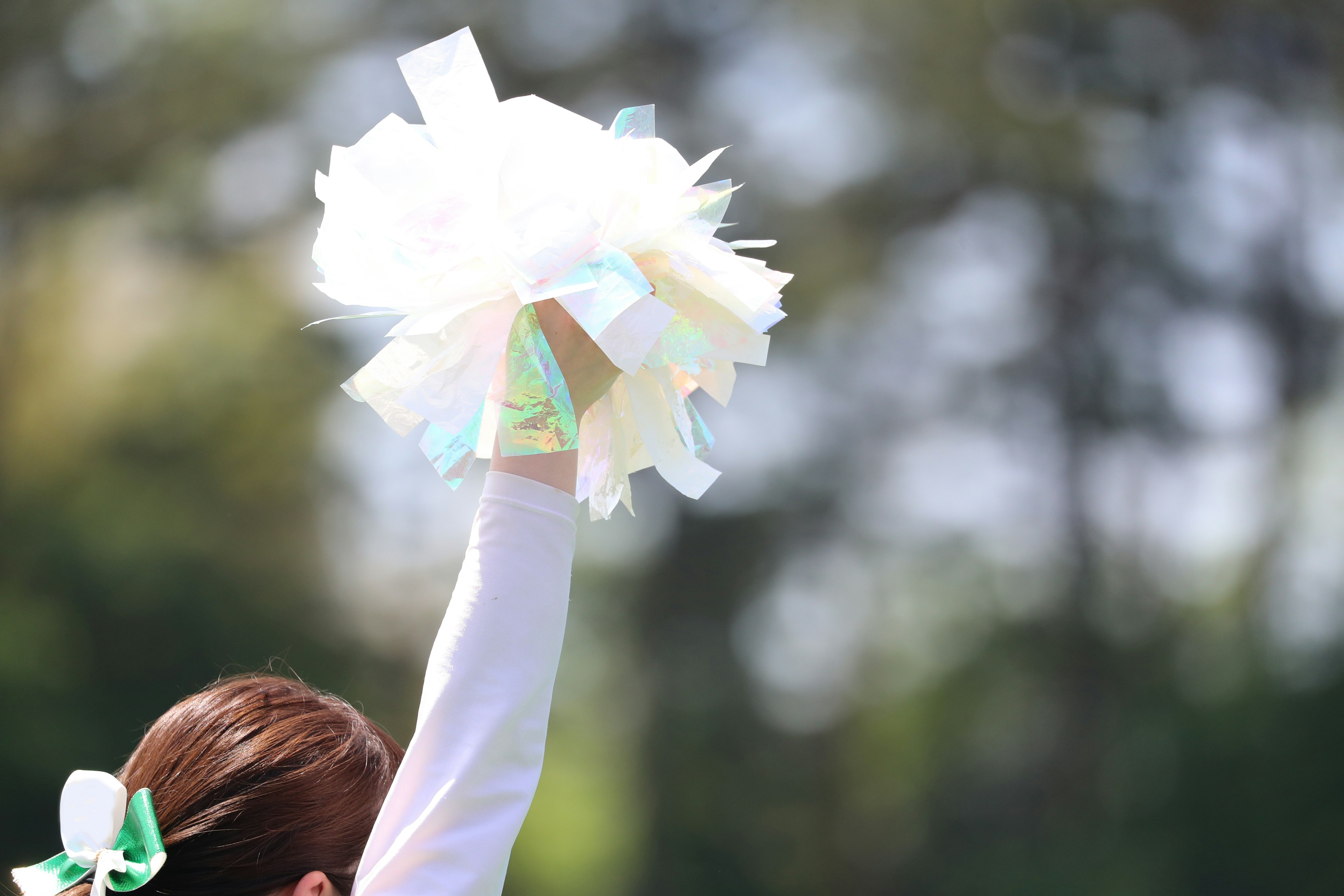 A cheerleader's hand holding colorful pom-poms