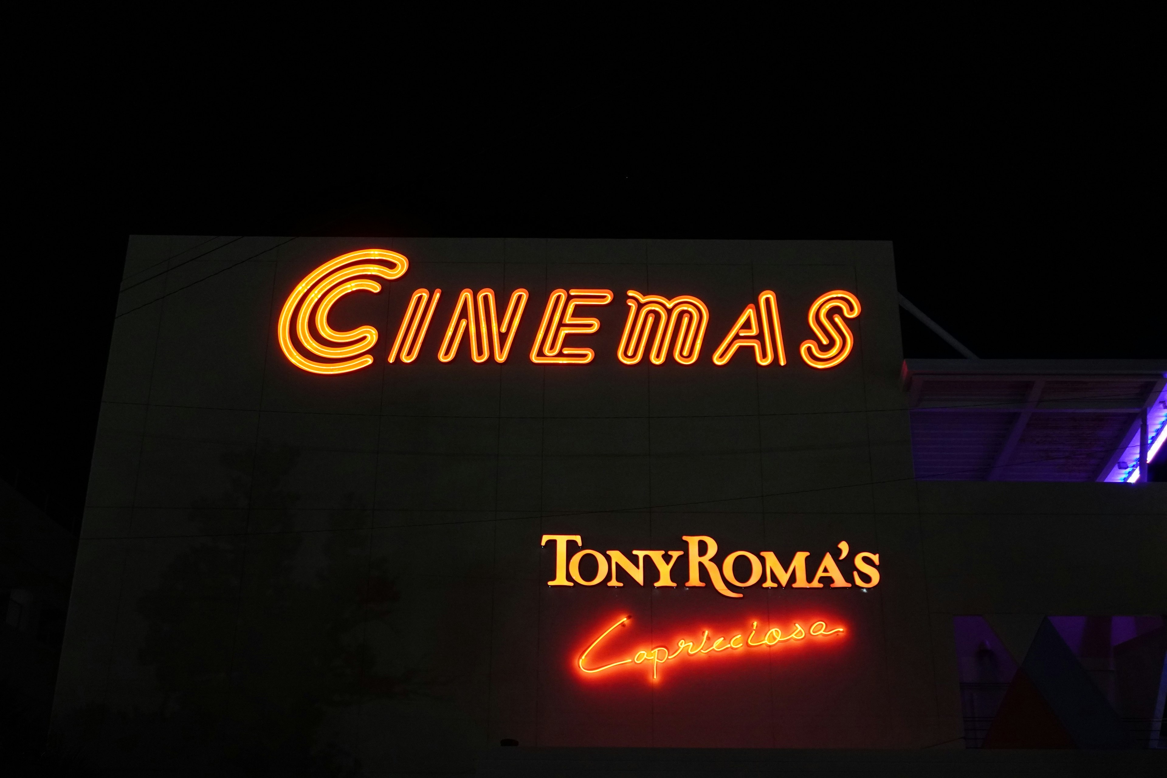 Cinema sign illuminated at night with Tony Roma's restaurant sign