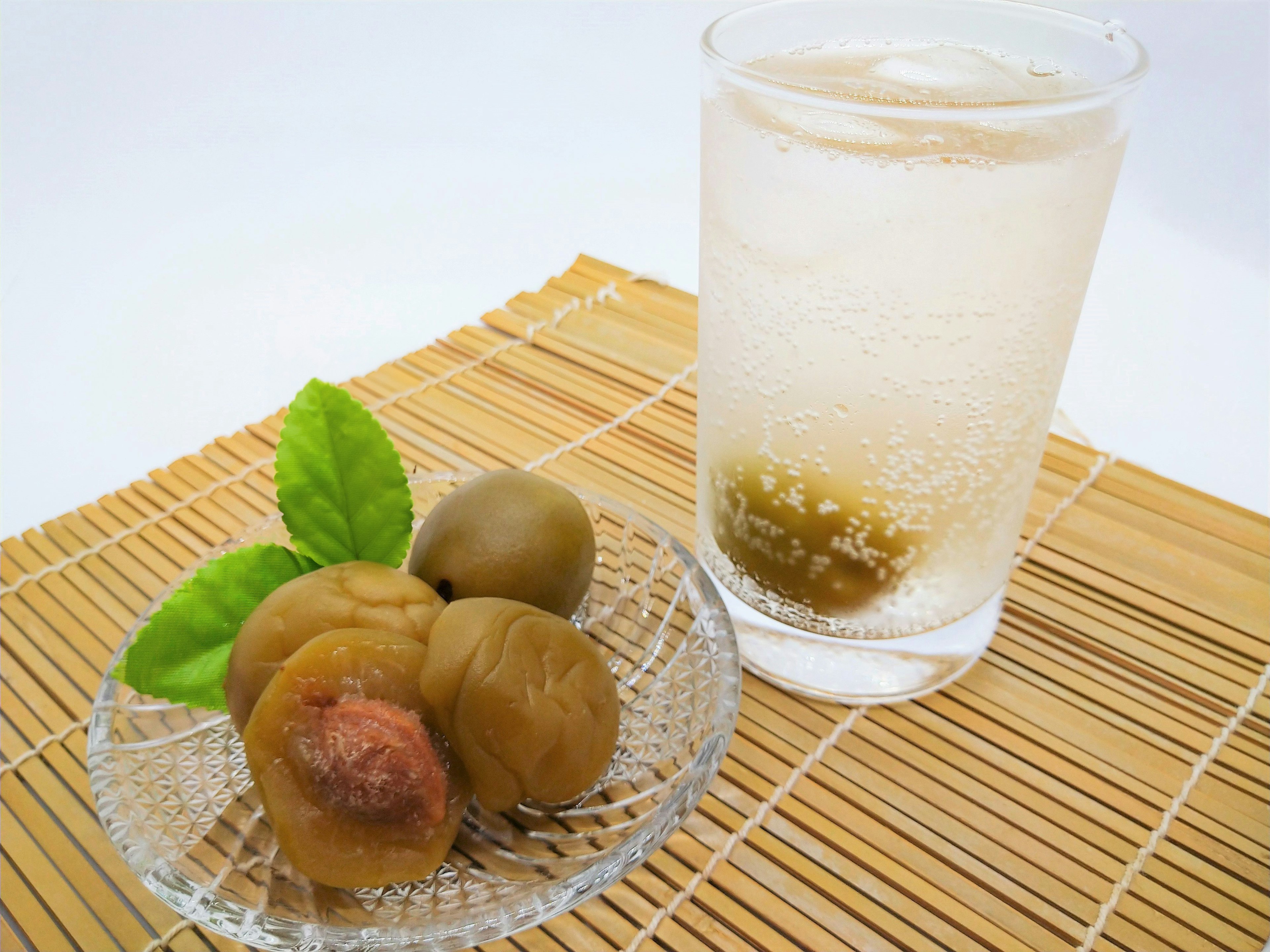 A glass of sparkling drink next to a dish of pickled plums and leaves