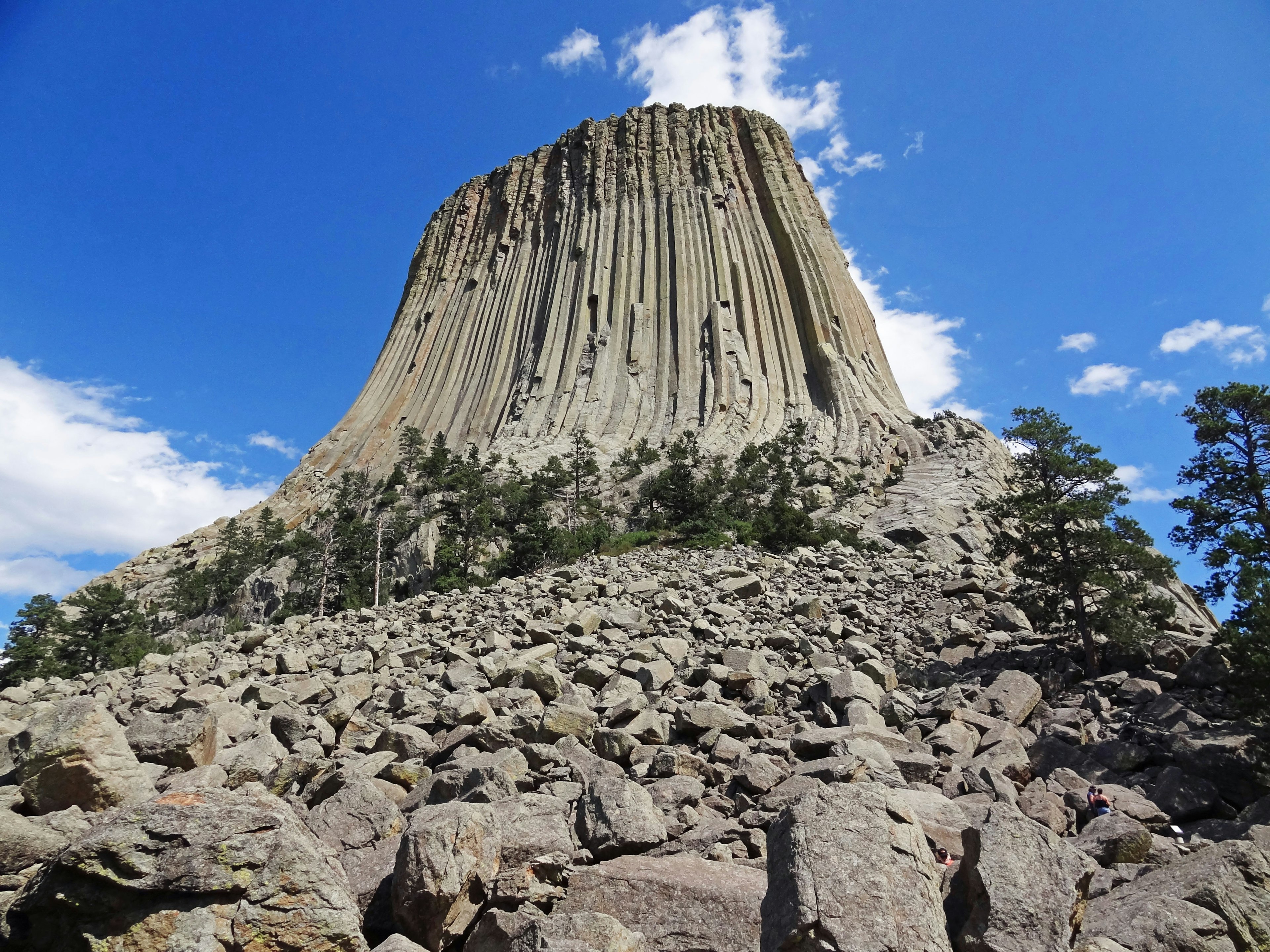 Formazione rocciosa drammatica simile a una torre con linee verticali circondata da massi sotto un cielo blu