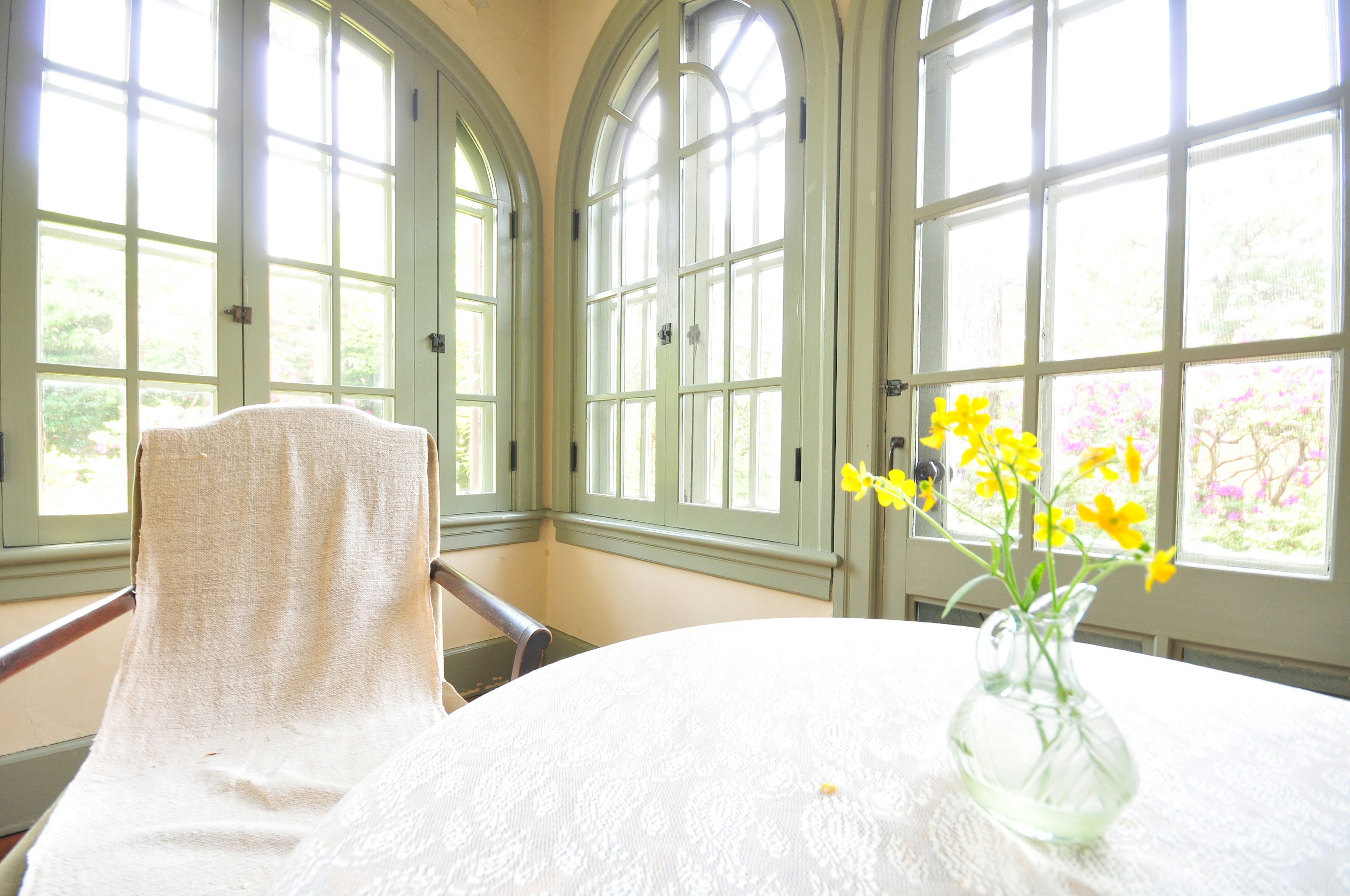 Brightly colored flowers in a vase on a table beside a chair with large windows