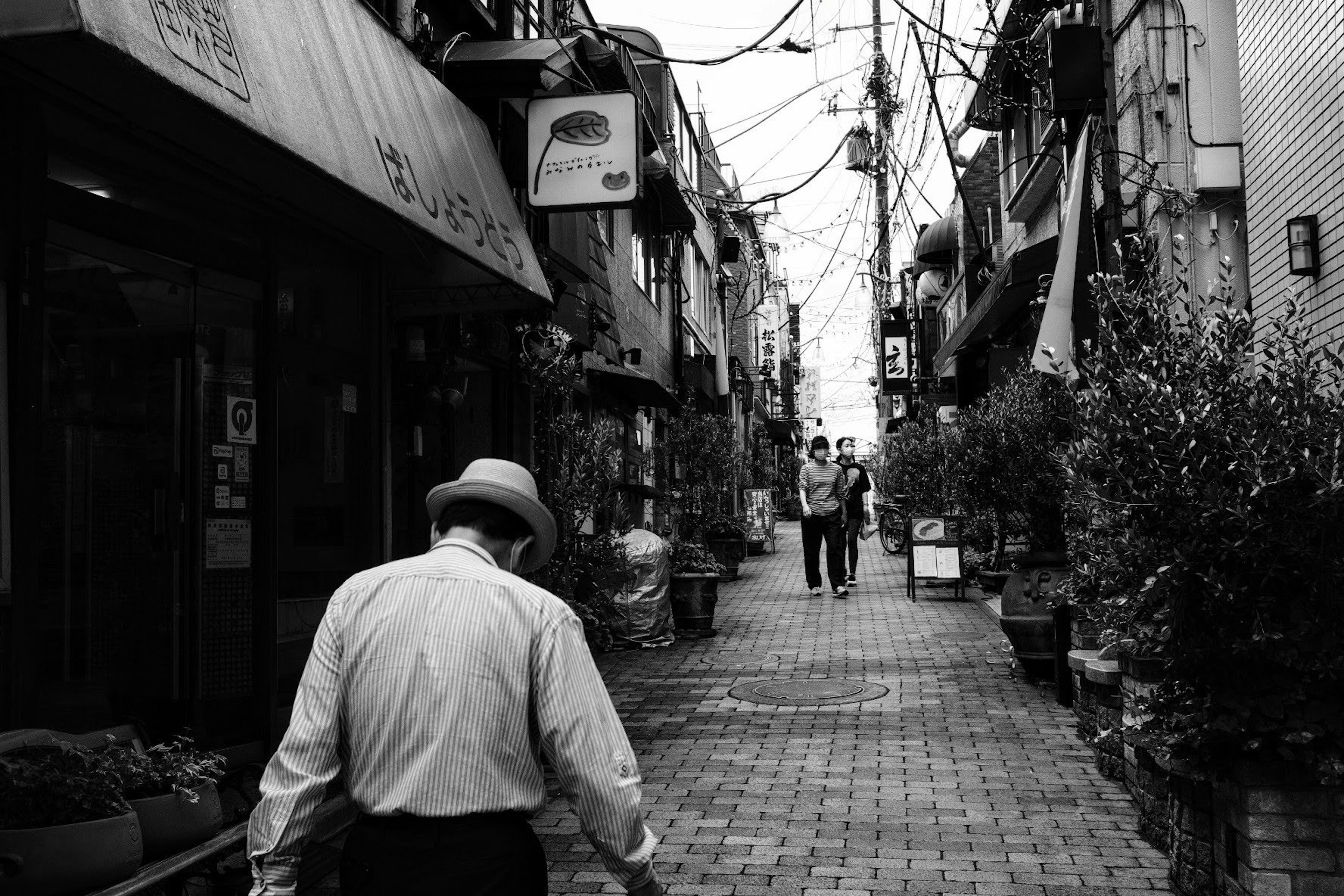 Un anciano caminando por un estrecho callejón en blanco y negro con otras personas