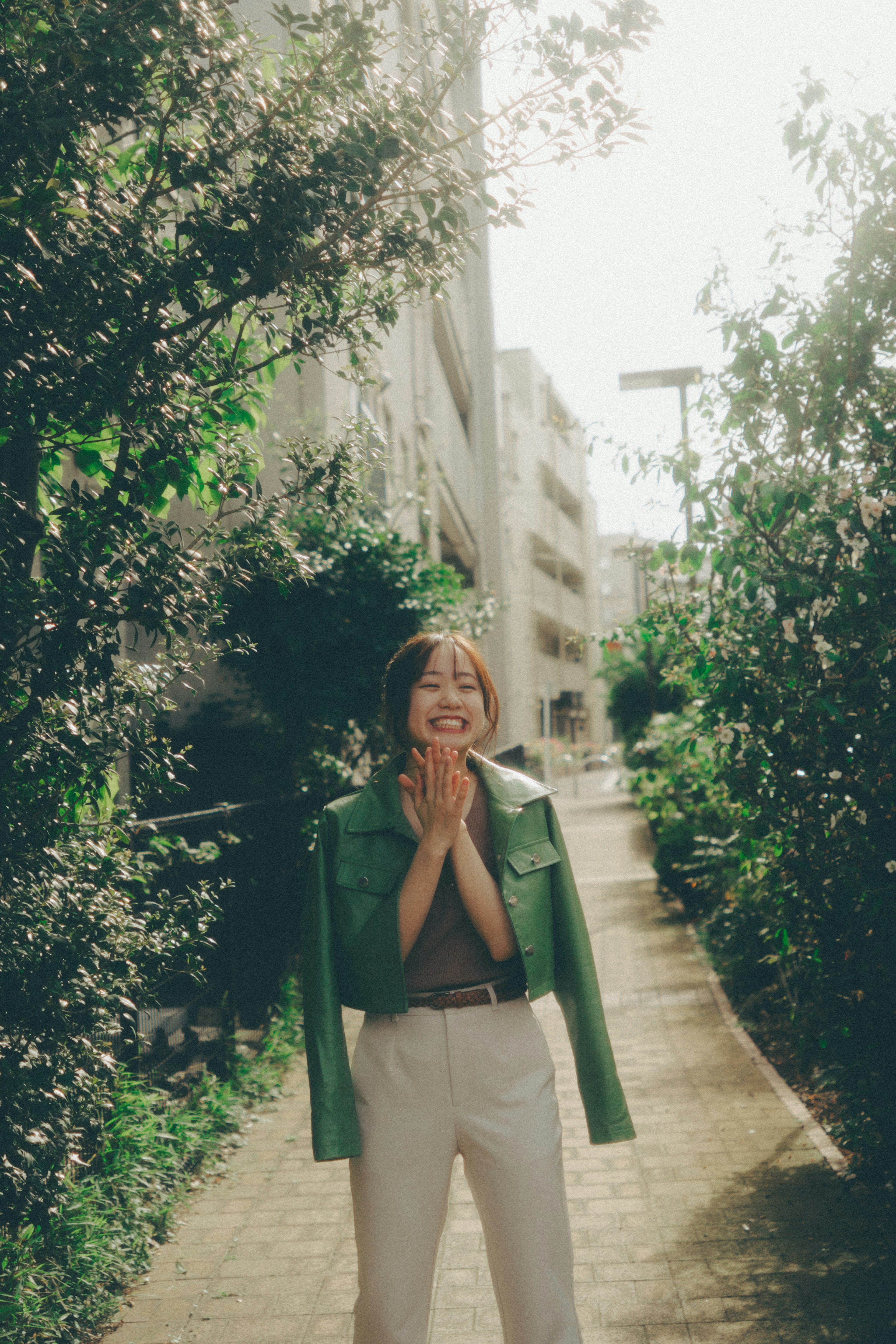 Una mujer sonriente con chaqueta verde está en un sendero rodeado de vegetación