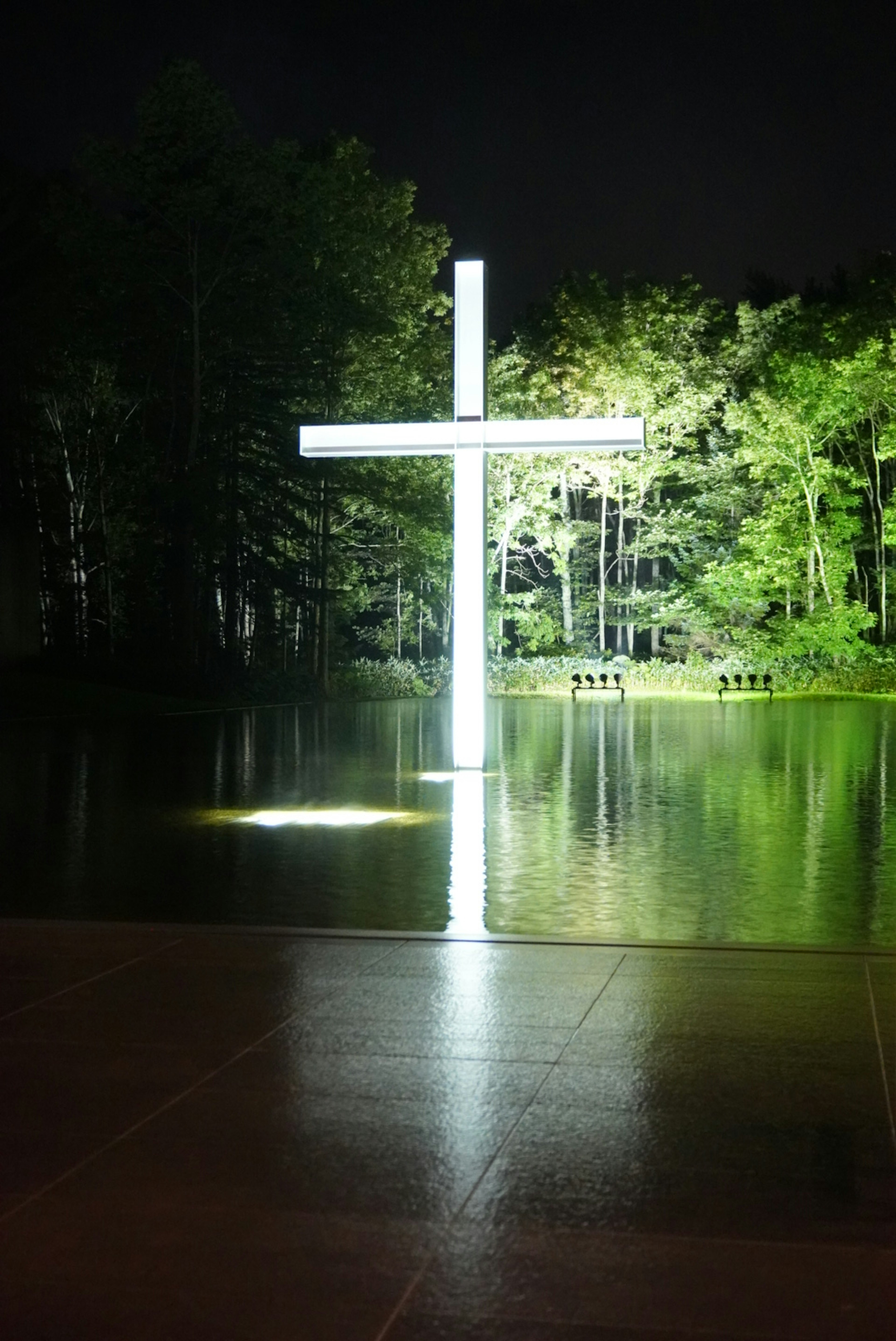 Großes weißes Kreuz, das nachts beleuchtet ist und sich auf der Wasseroberfläche spiegelt