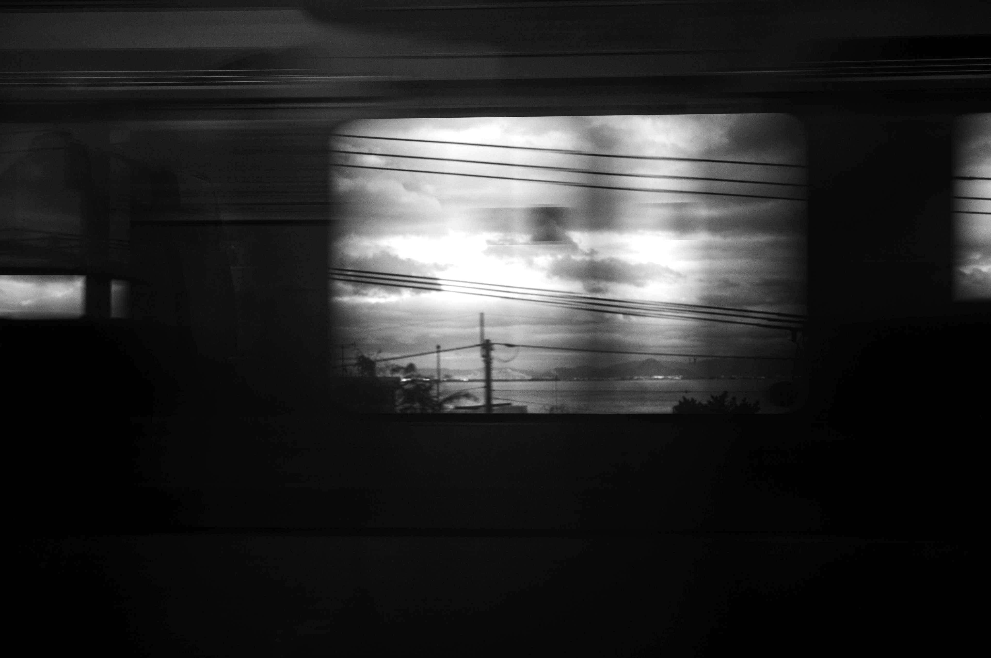 Black and white landscape viewed through a moving window showing clouds and a power pole