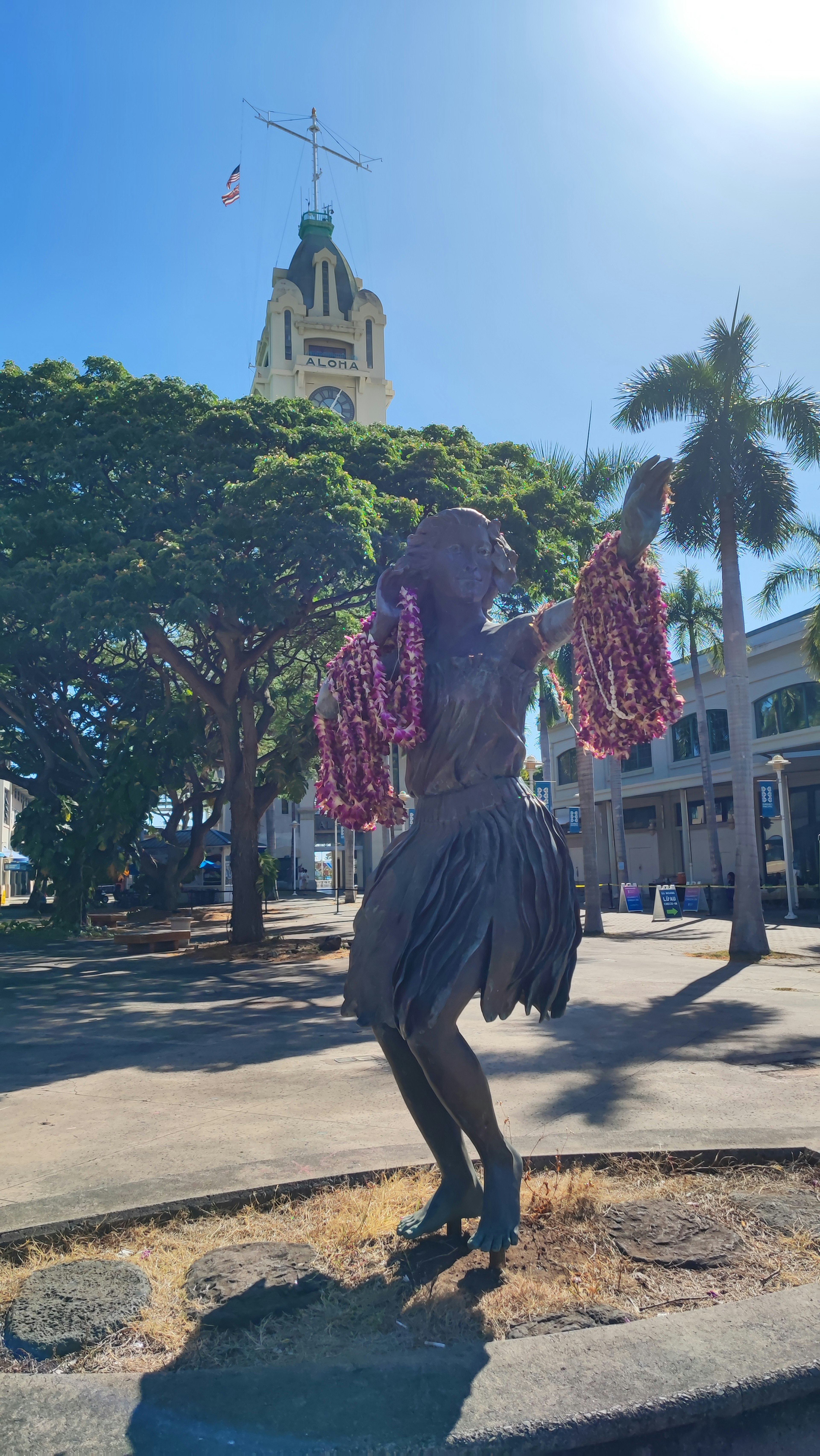 A woman performing a dance under sunlight with a tall tower and green trees in the background