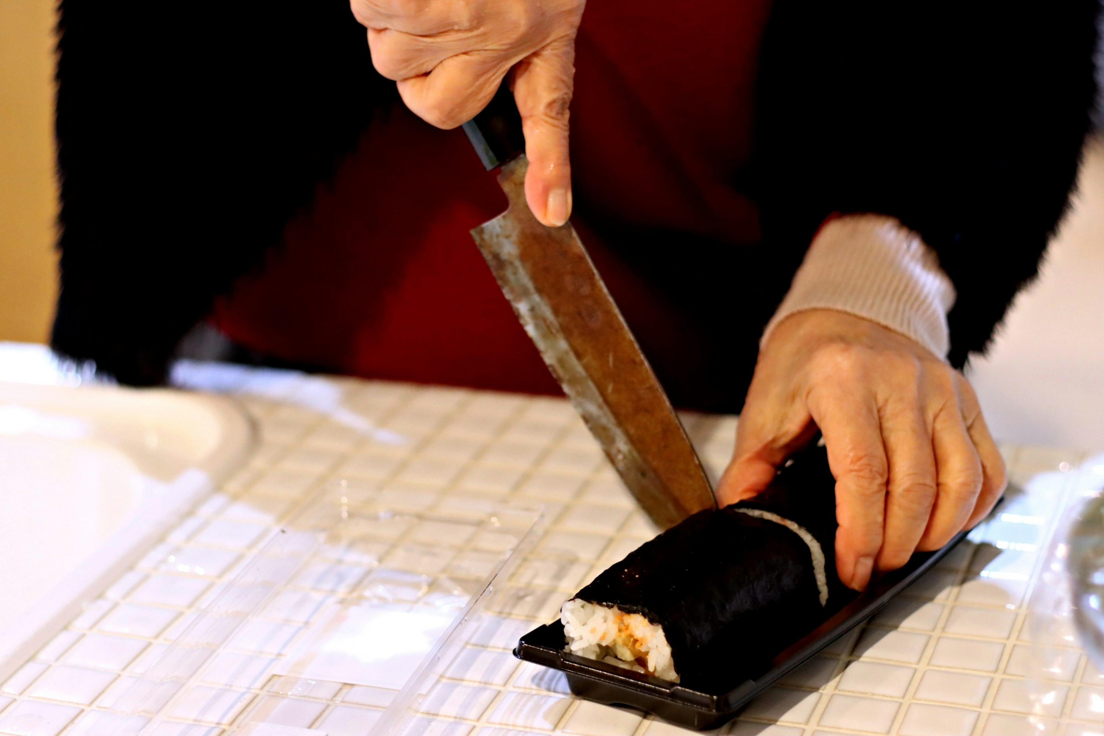 Hände schneiden eine Sushi-Rolle mit einem Messer auf einer weißen Oberfläche