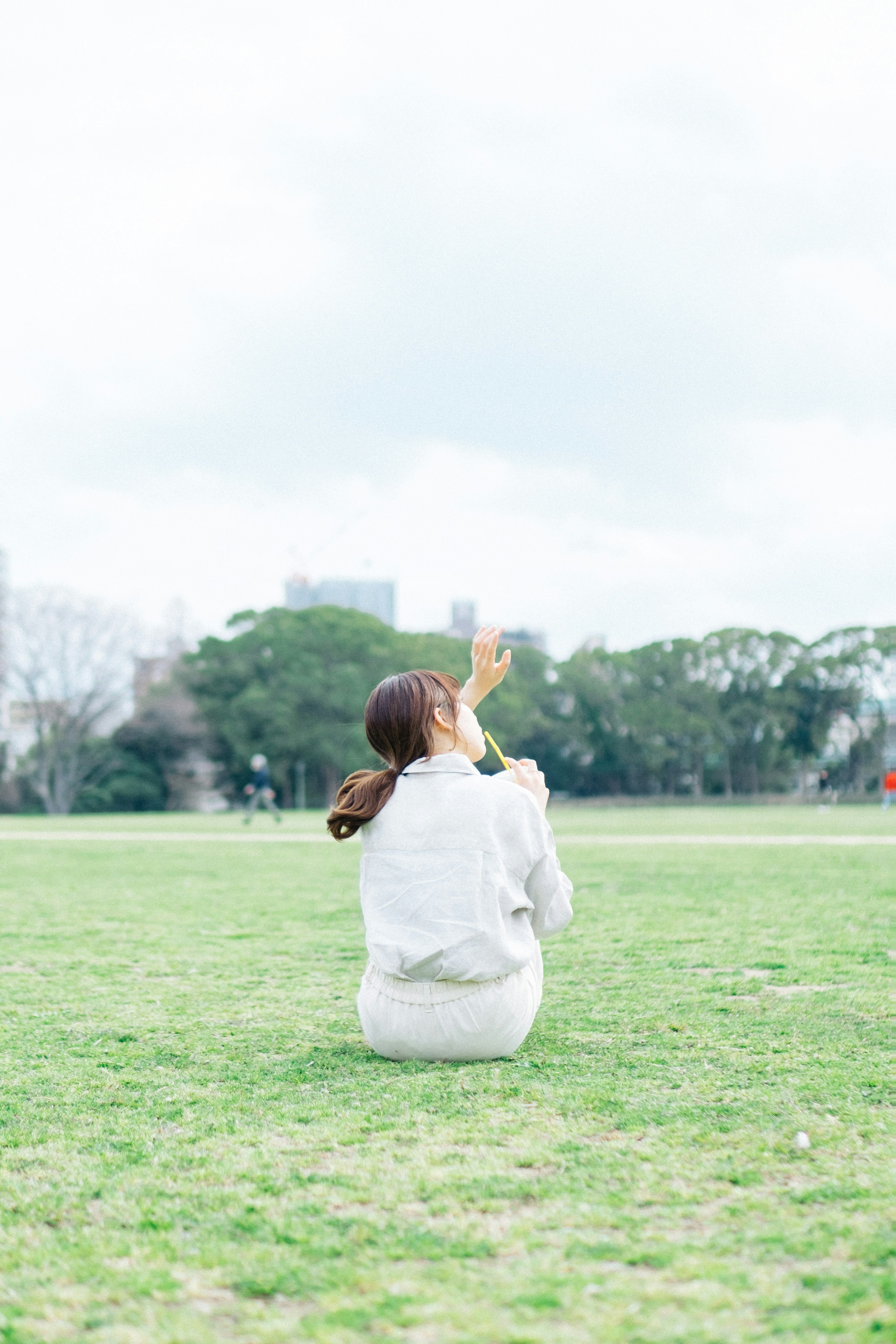 公園で後ろ向きに座る女性 白い服と緑の草地の背景