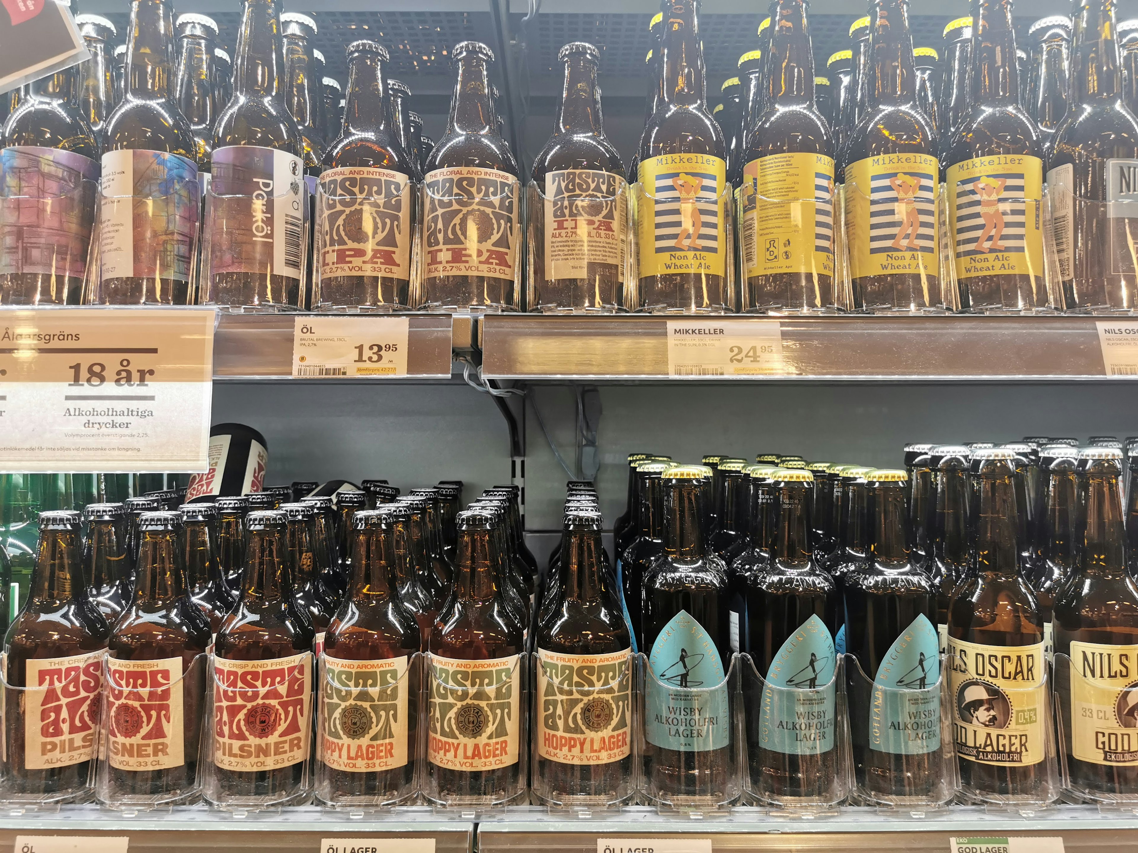 Imagen de una estantería llena de varias botellas de cerveza La fila superior presenta botellas etiquetadas mientras que la fila inferior muestra botellas etiquetadas diferentes