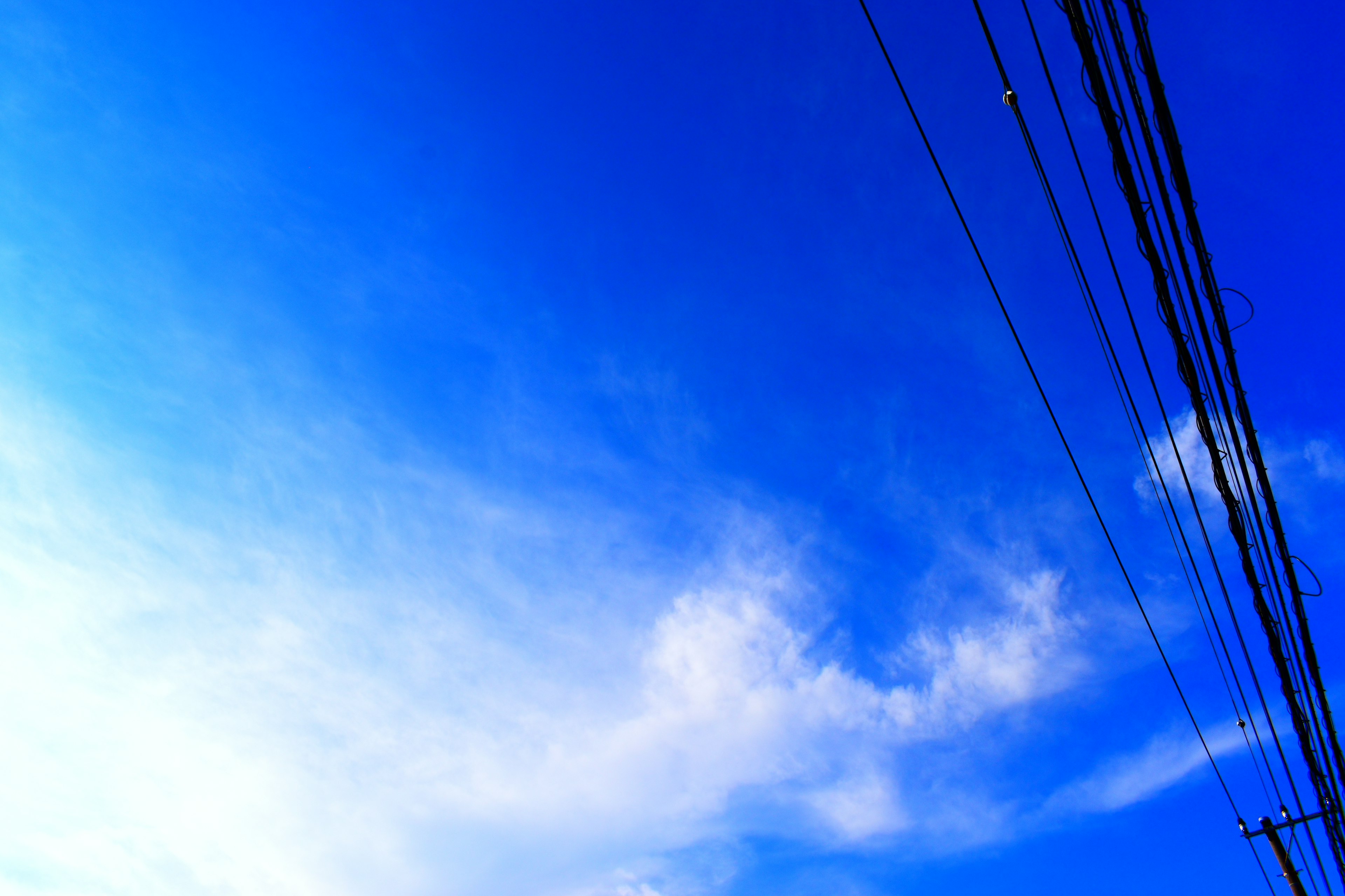 Ein Foto eines blauen Himmels mit Wolken und sichtbaren Stromleitungen