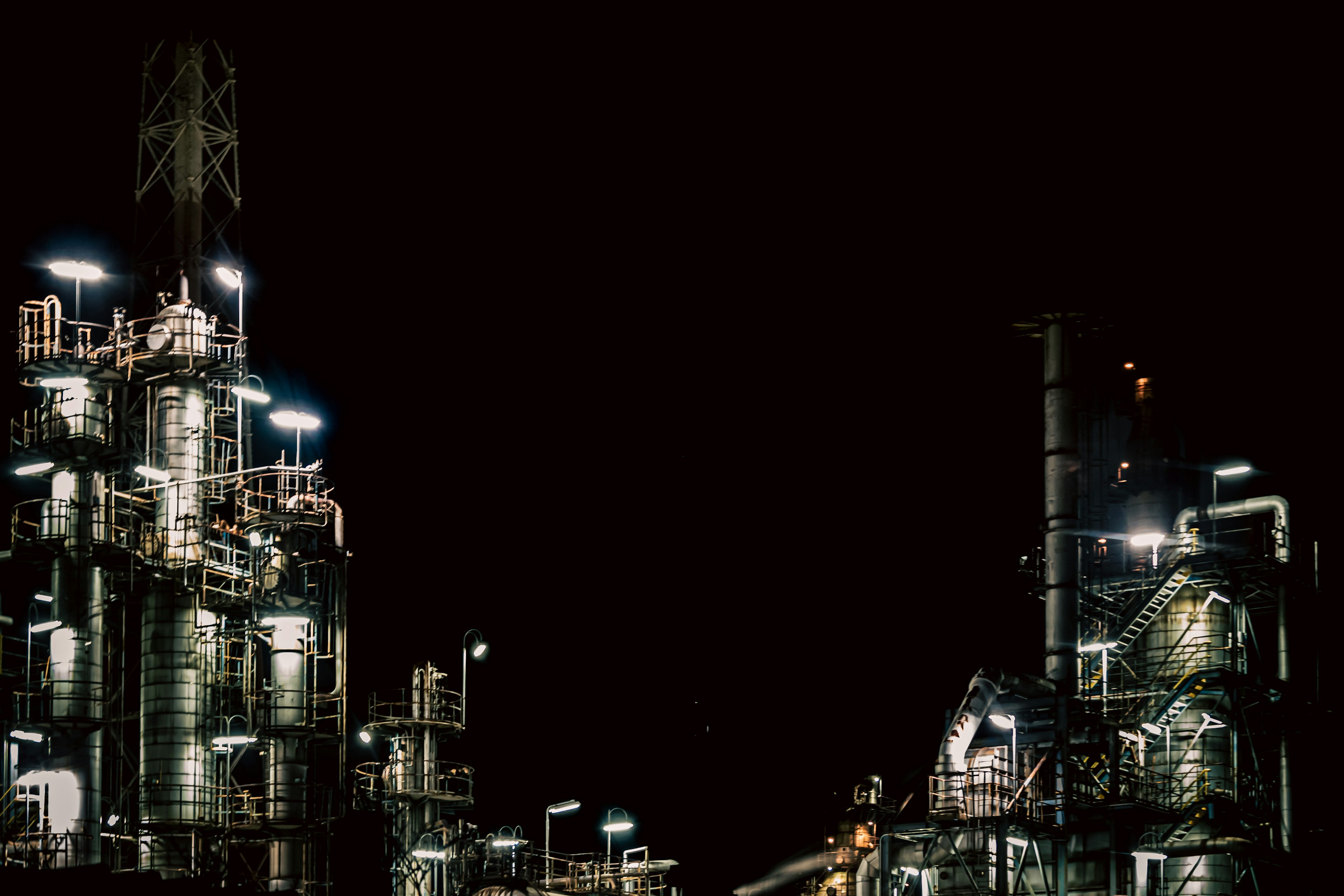 Night view of industrial facility with illuminated tanks and smokestacks