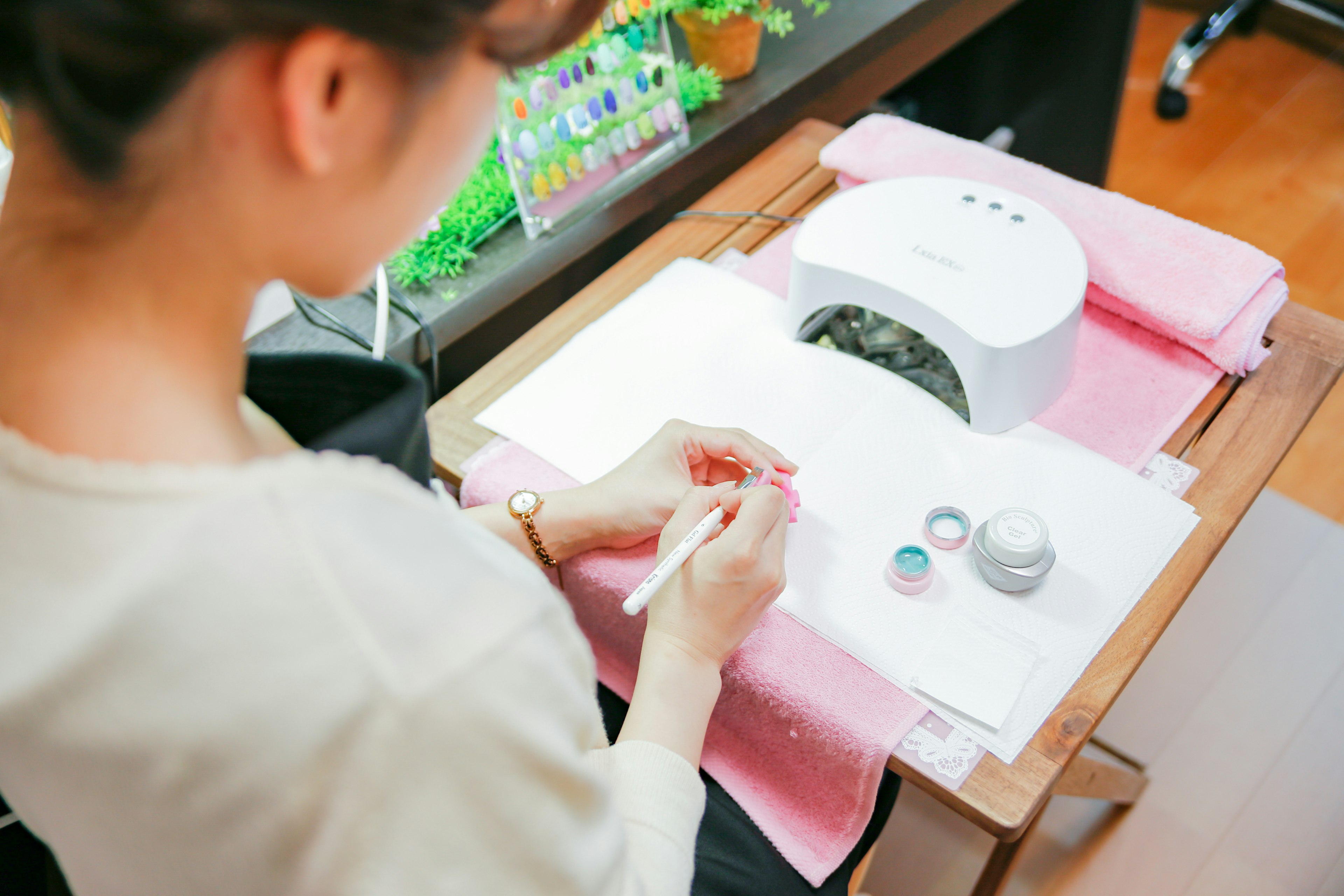 Mujer aplicando arte de uñas con suministros y lámpara UV en una mesa de trabajo