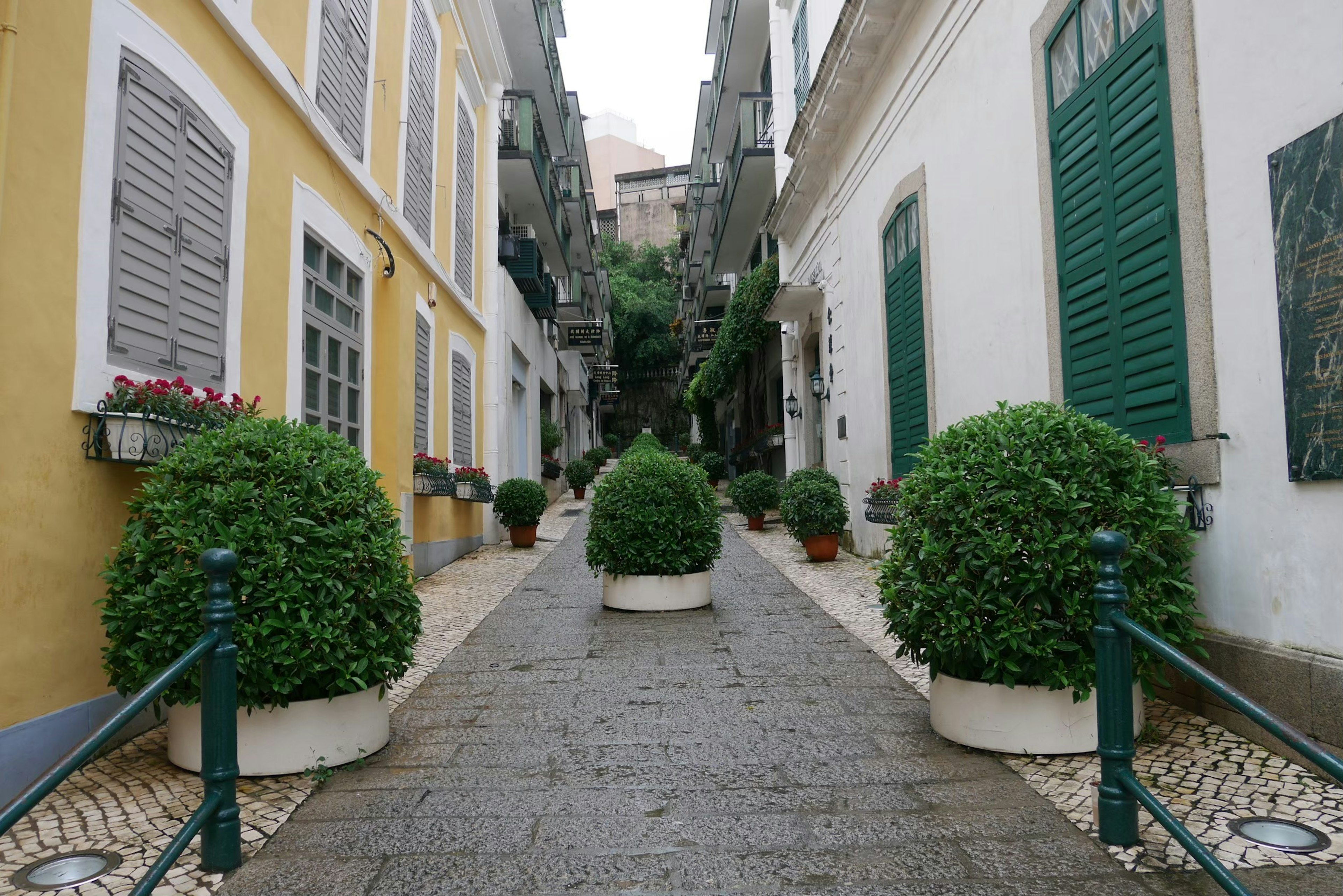 Narrow street lined with yellow and white buildings and round planters