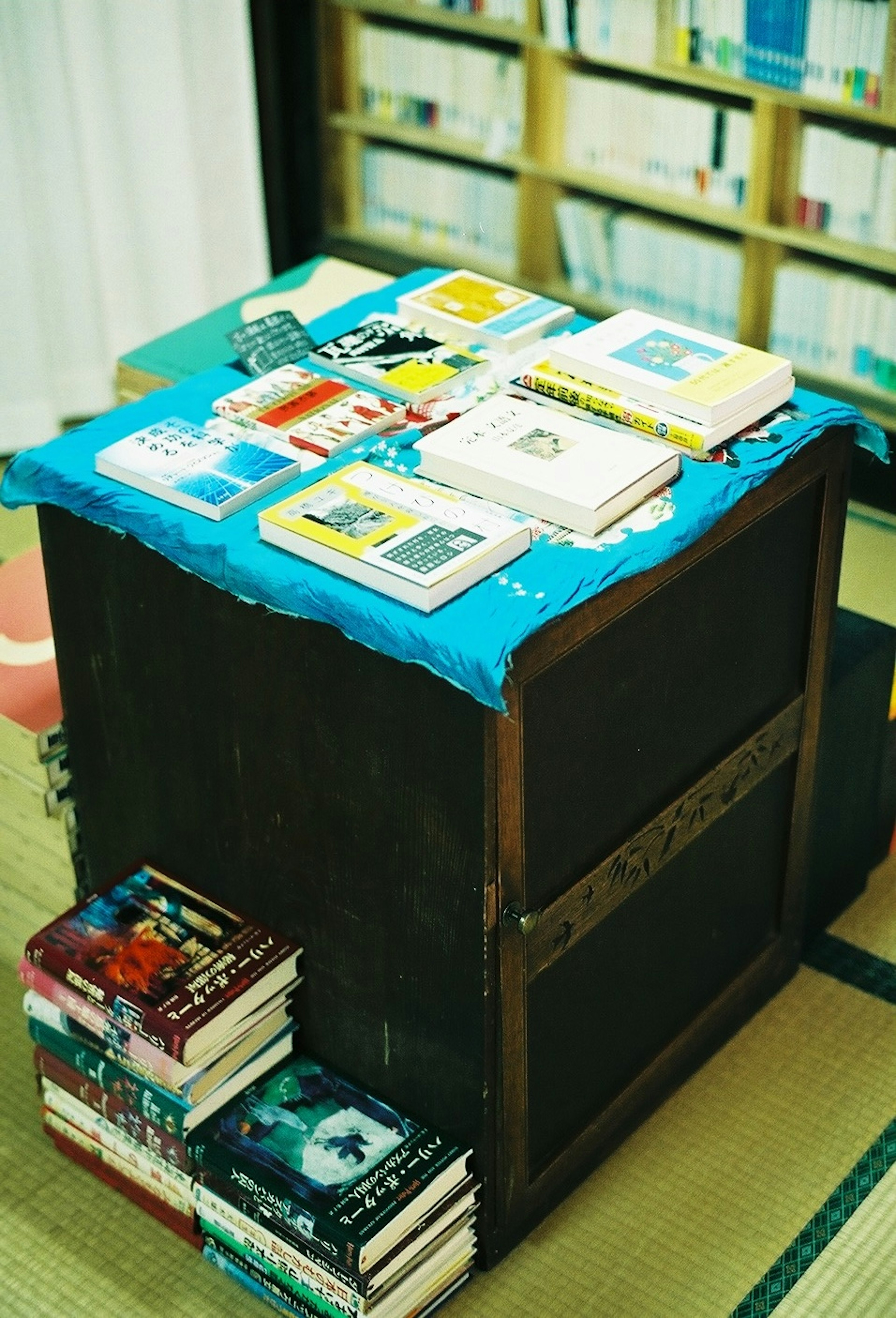 Wooden table covered with a blue cloth displaying various books on top and stacked books around