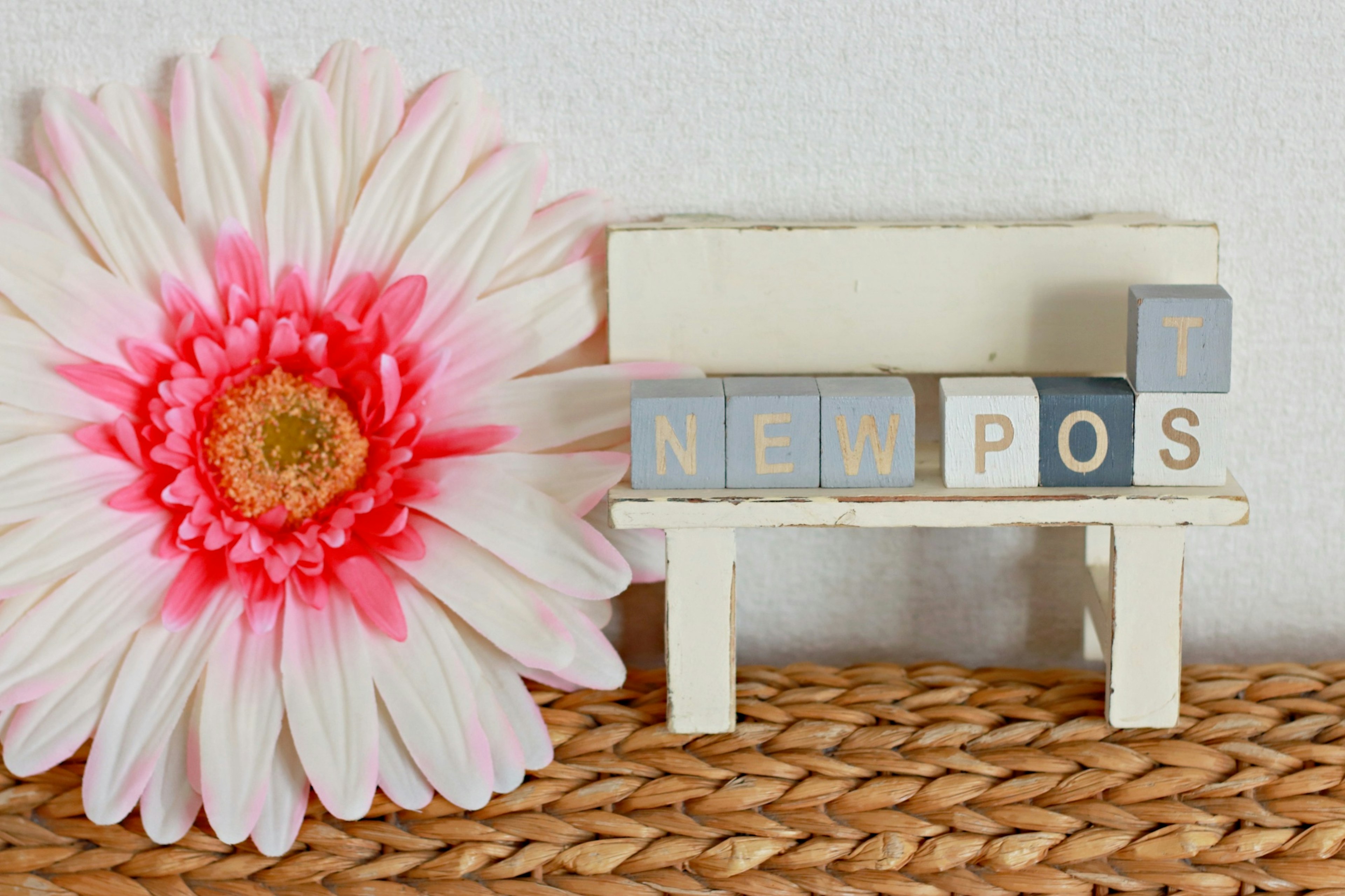 A small white bench with blocks spelling 'NEW POST' next to a large pink flower