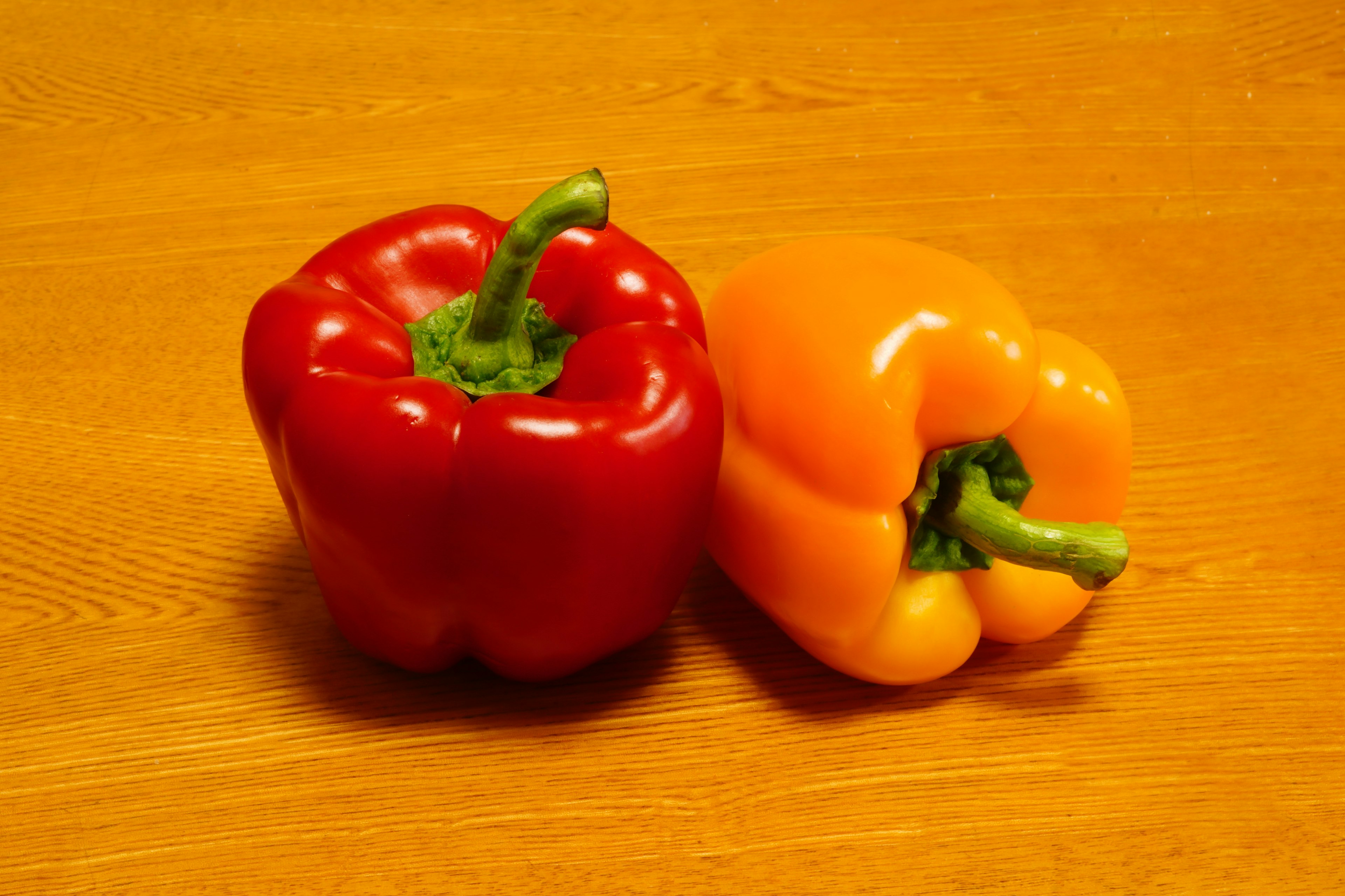 Red and orange bell peppers placed on a wooden table