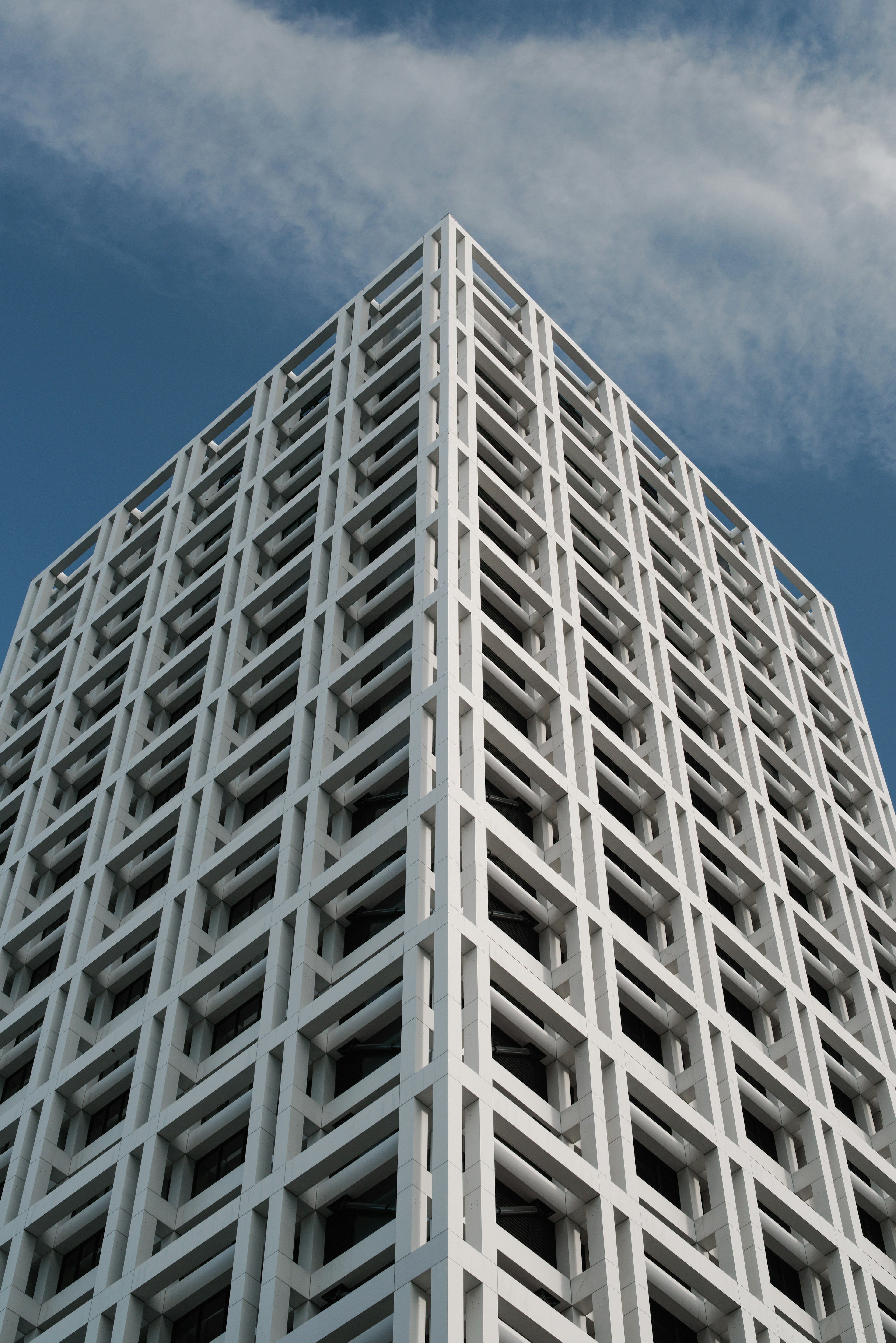 Vista de un edificio de concreto blanco desde un ángulo que muestra su diseño único y el cielo con nubes