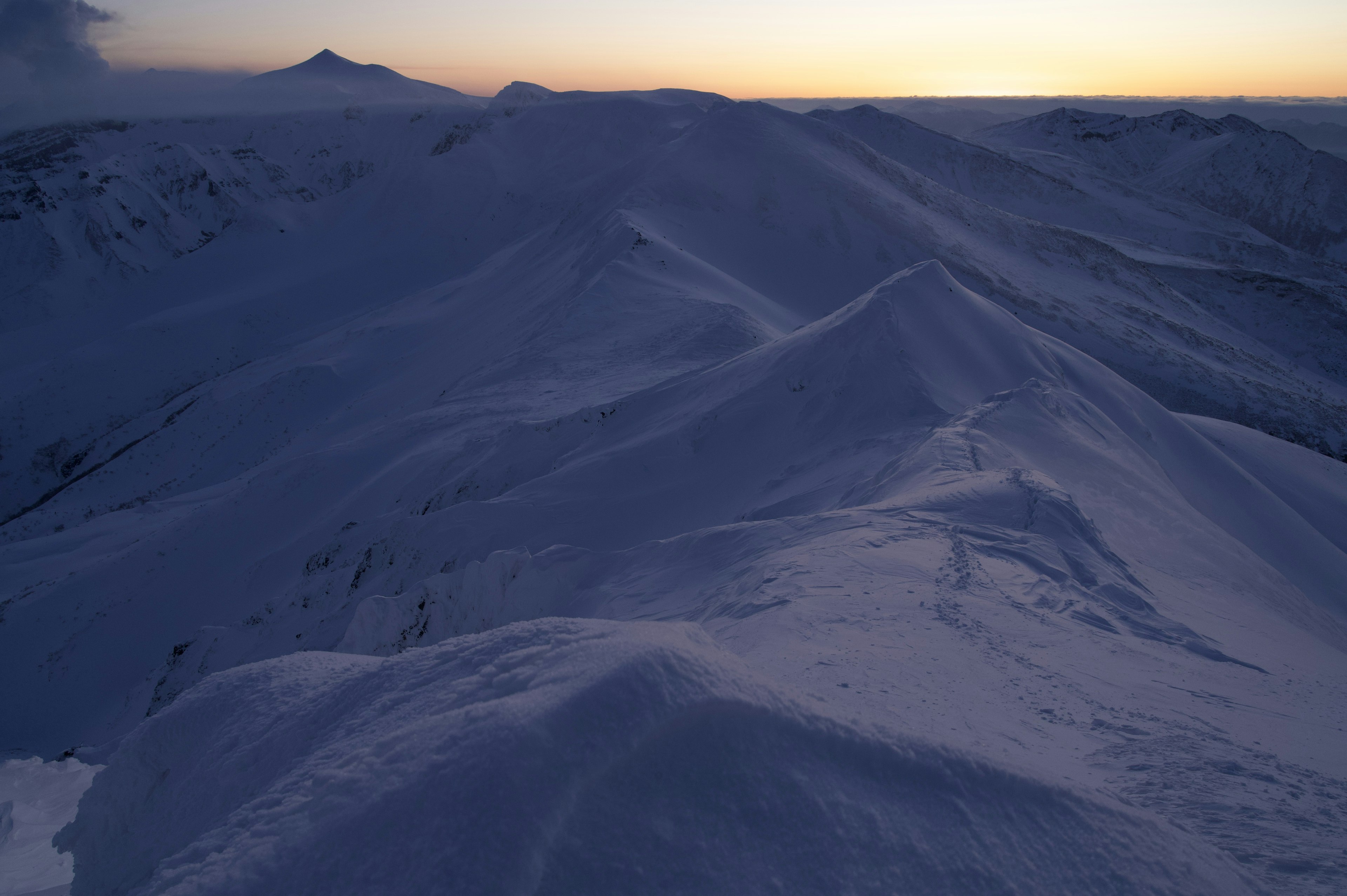 雪に覆われた山々の広がりと夕日の柔らかい光