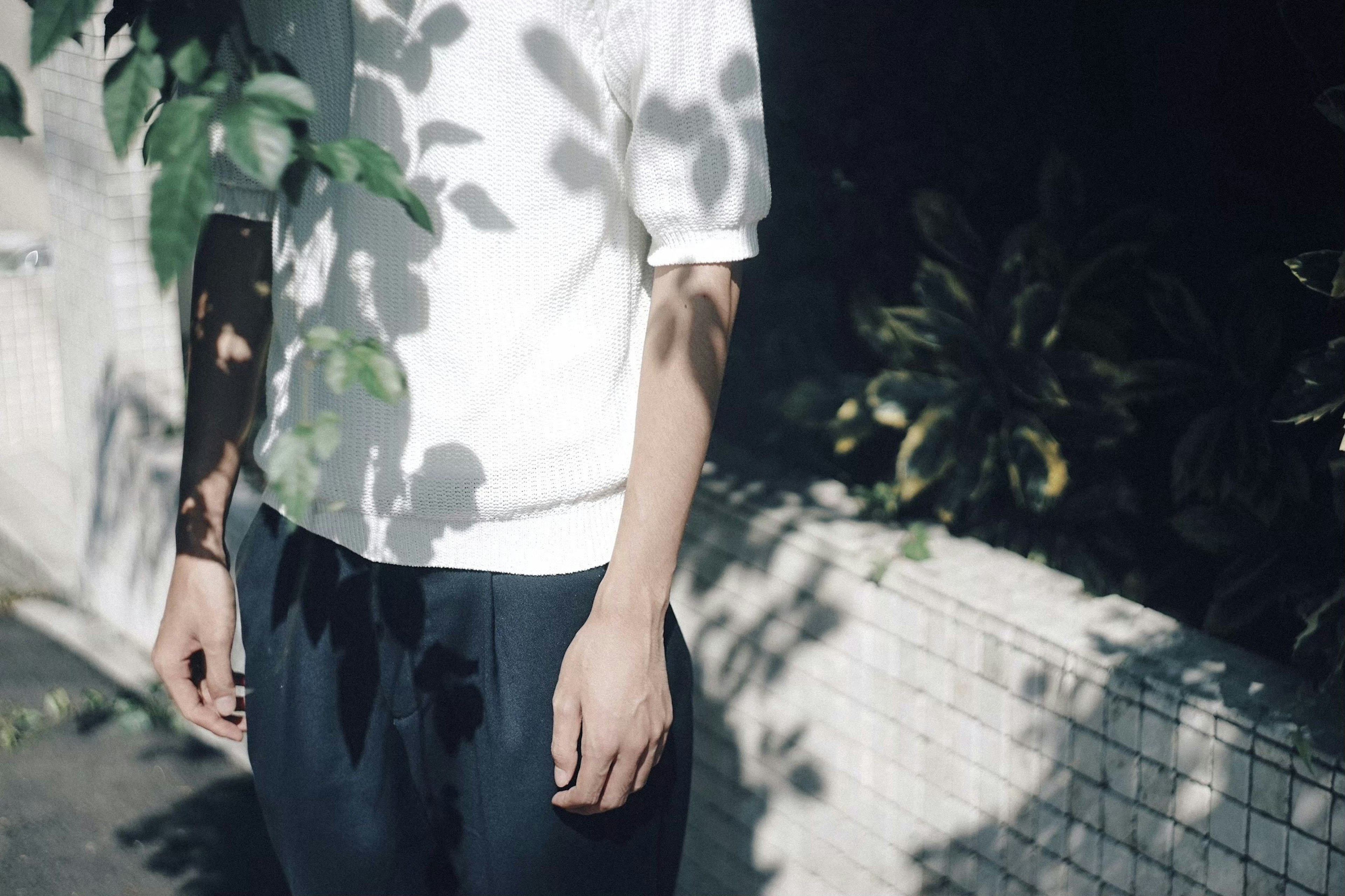 A man wearing a white shirt with visible arms and hands, shadows of leaves falling on him