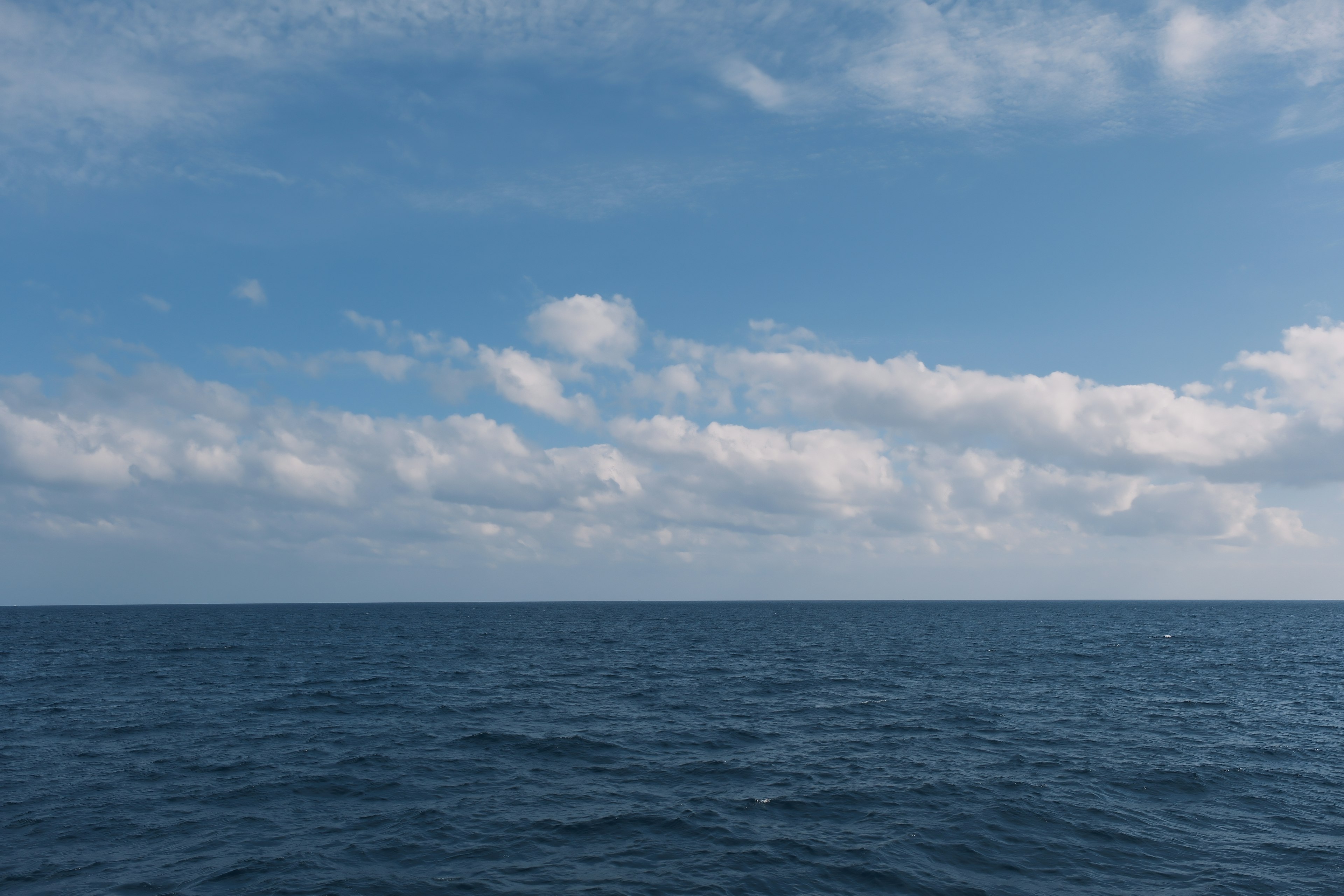 Océan bleu avec un ciel dégagé et des nuages blancs