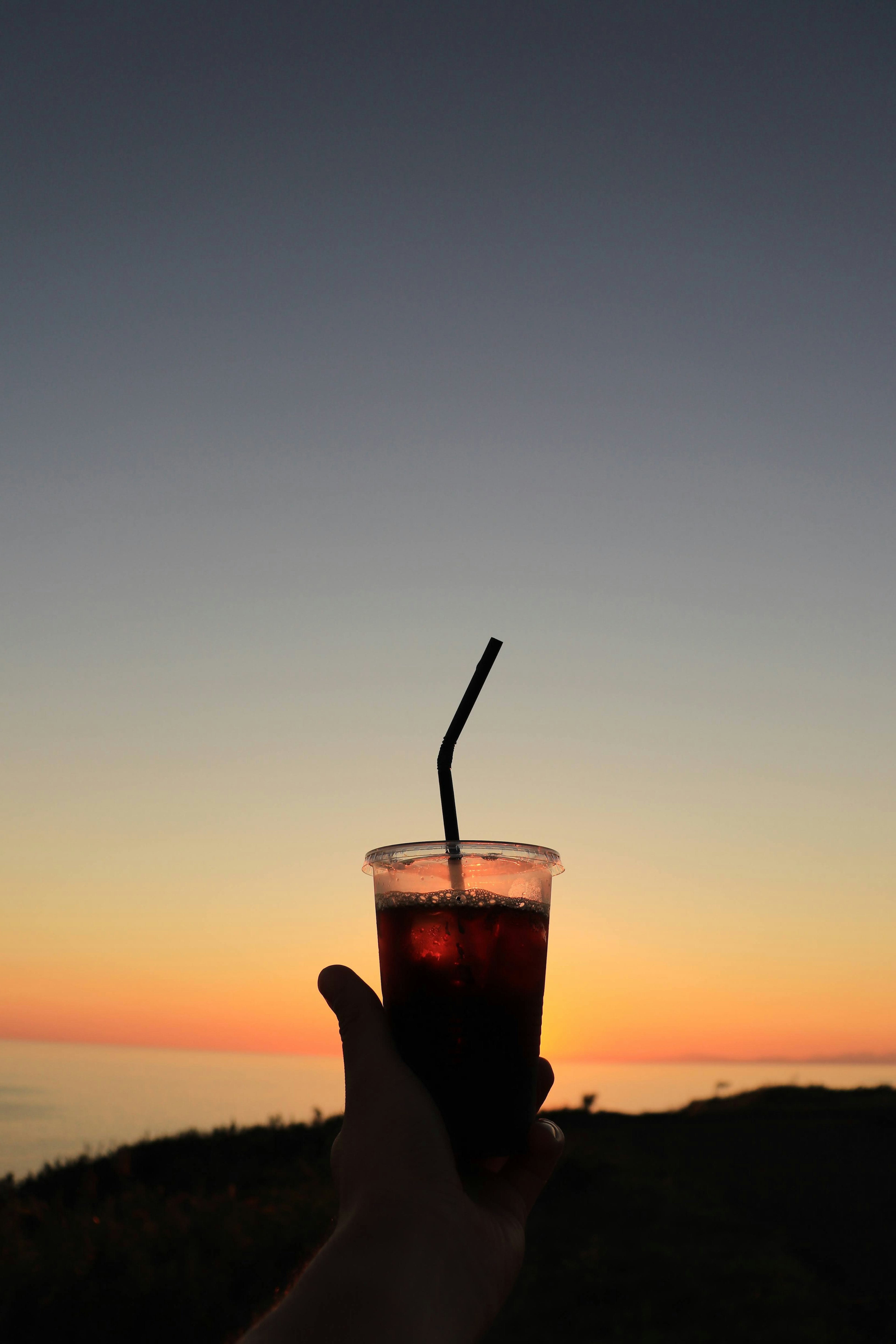 Tangan memegang gelas minuman dengan latar belakang matahari terbenam