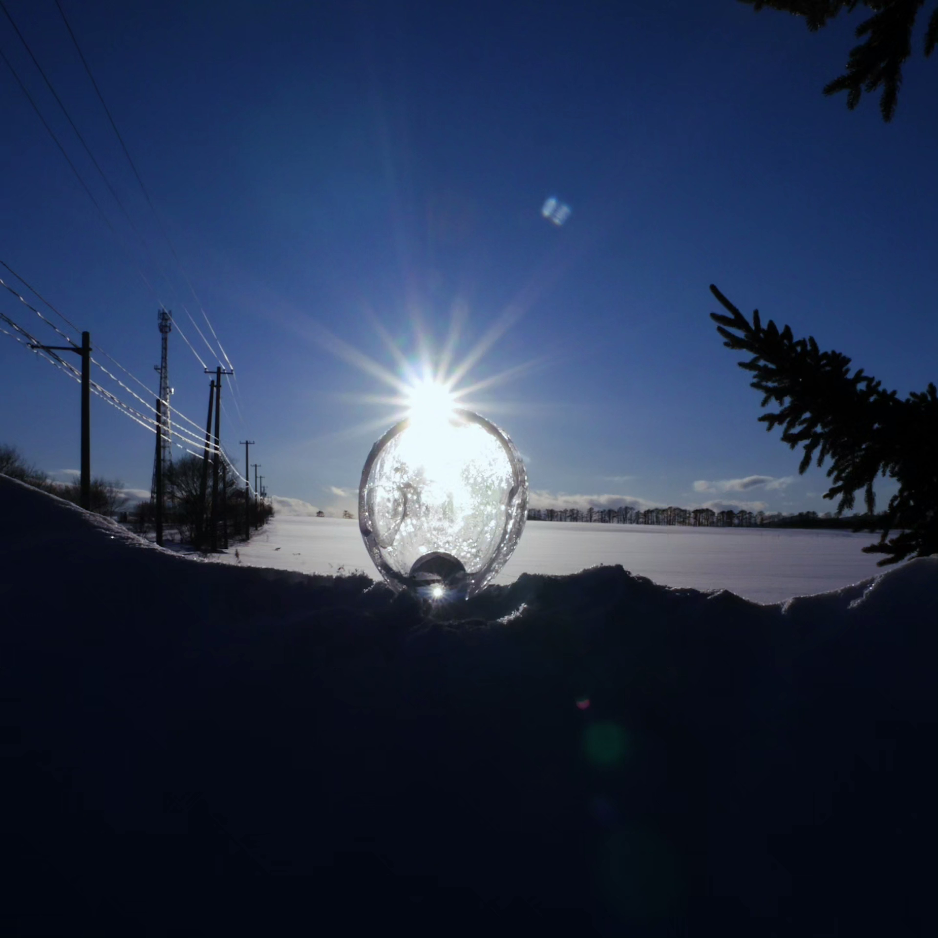 雪に覆われた風景の中に輝く太陽の光が映る透明な球体