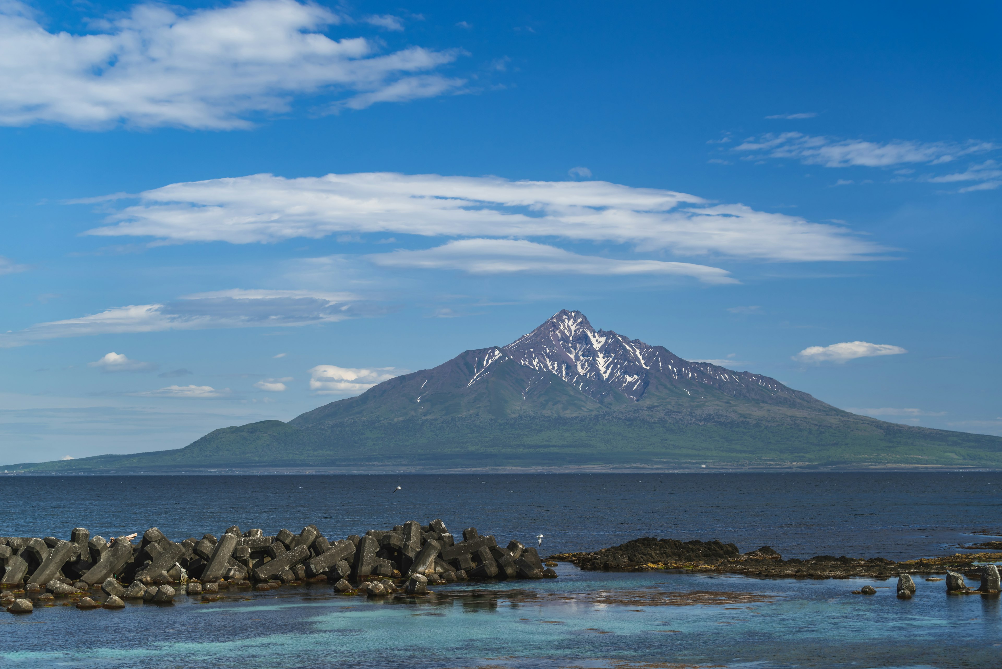 Mont enneigé s'élevant sous un ciel bleu avec des nuages Pentes vertes et mer bleue au premier plan